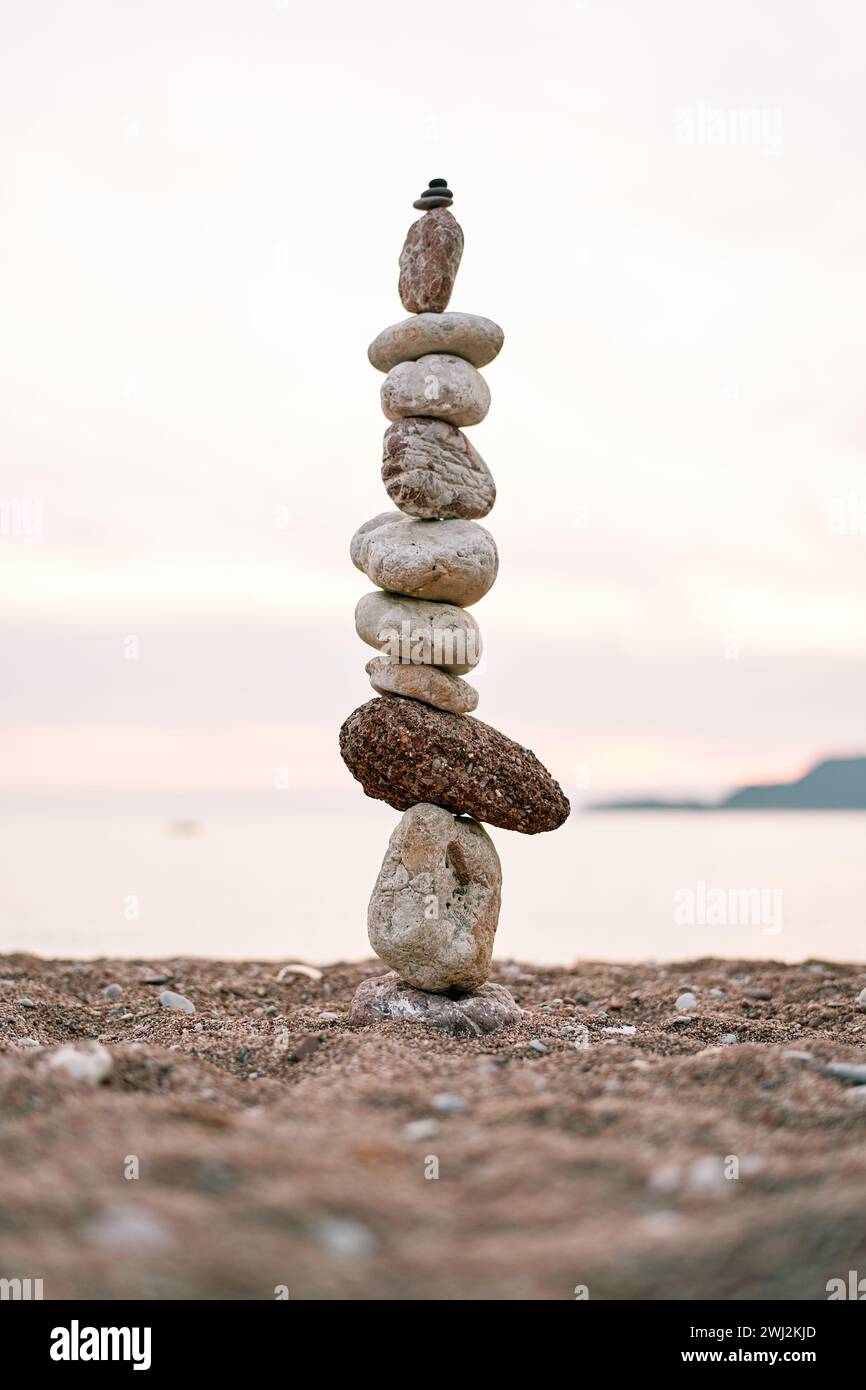 Cairn si erge sulla riva del mare al tramonto rosa Foto Stock