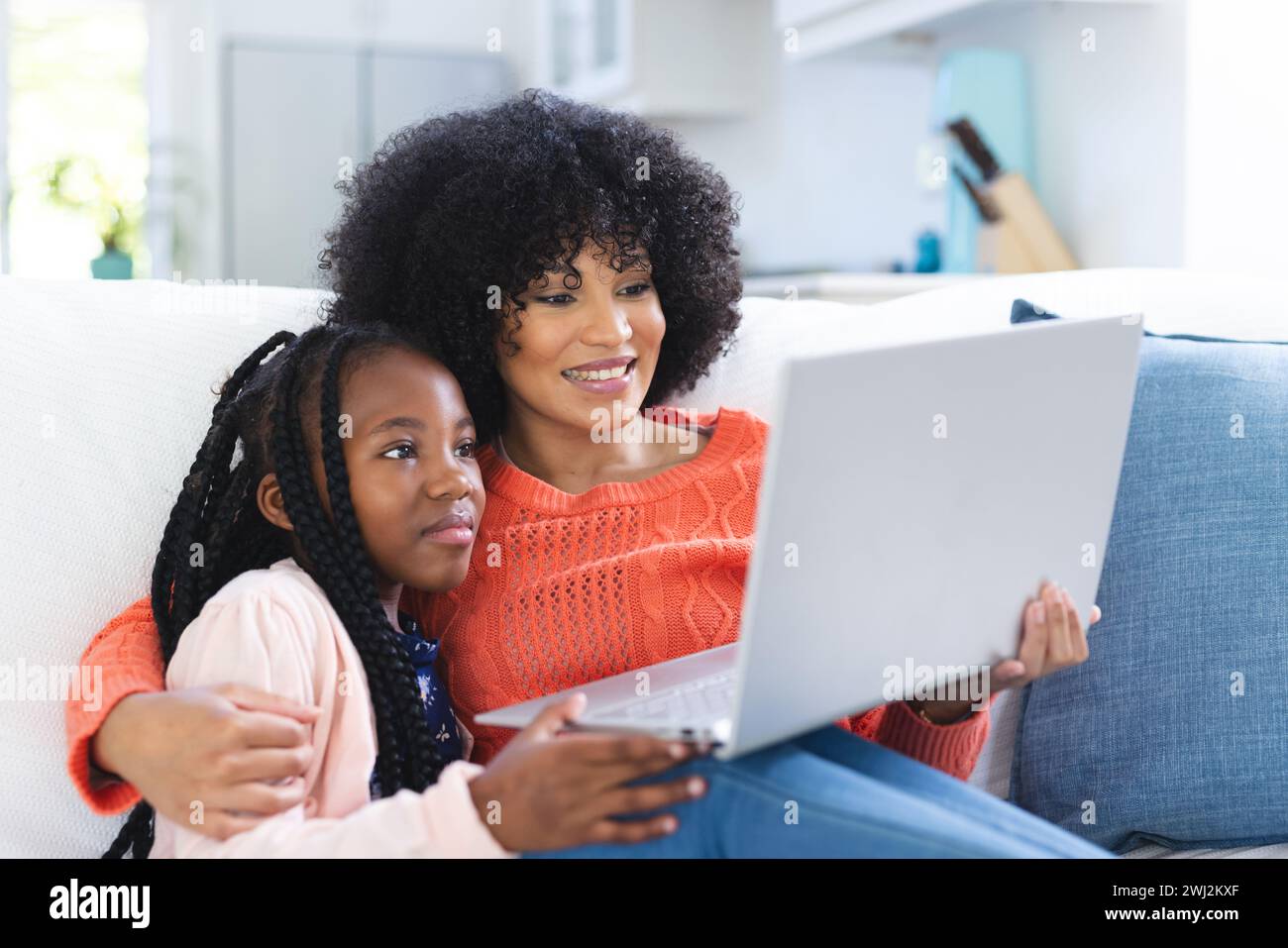 Madre e figlia afroamericana felici che abbracciano sul divano e usano il computer portatile a casa, spazio di copia Foto Stock