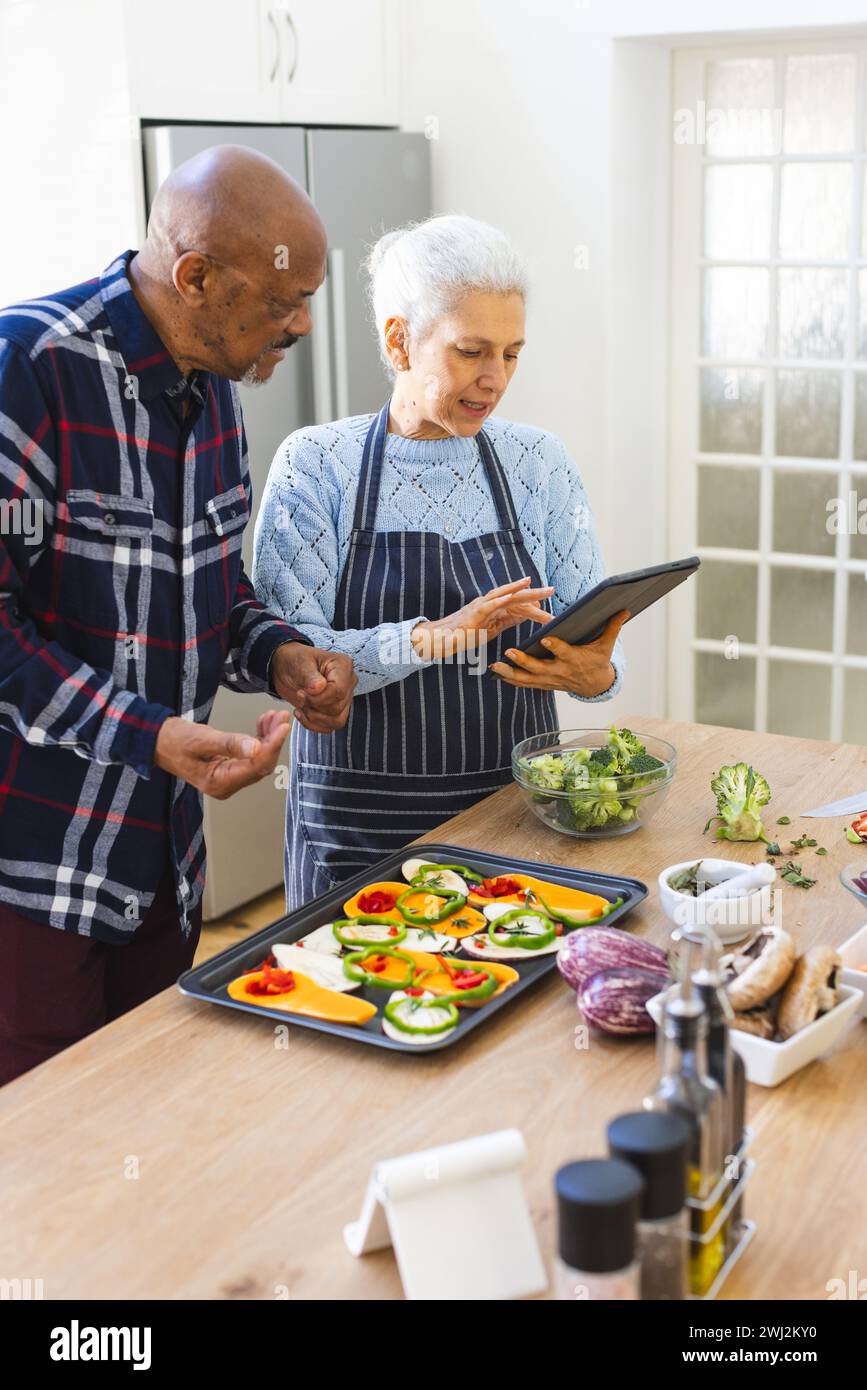 Diverse coppie anziane preparano il pasto utilizzando un tablet in cucina Foto Stock