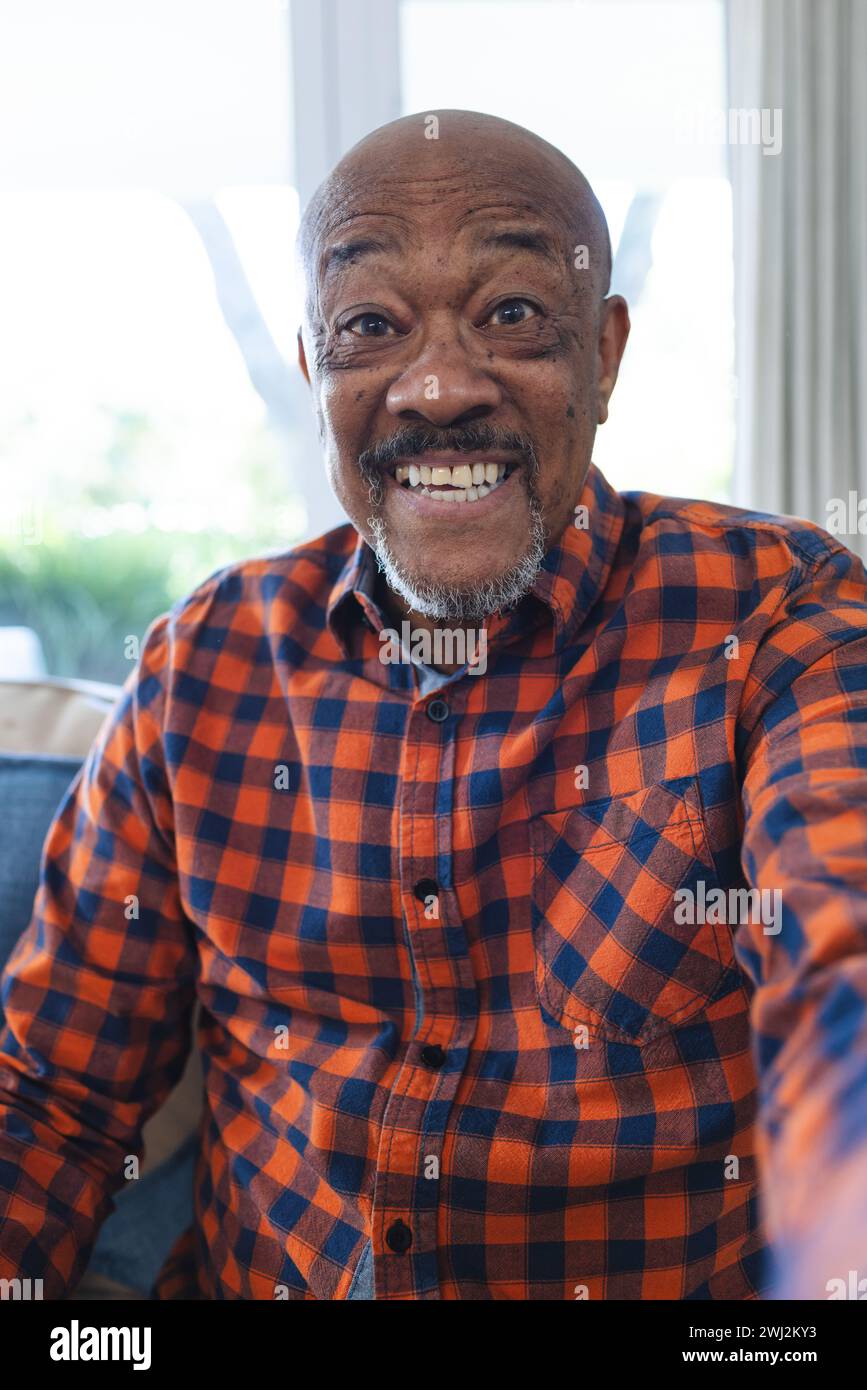 Felice uomo anziano afroamericano che fa videochiamate in un soggiorno soleggiato Foto Stock