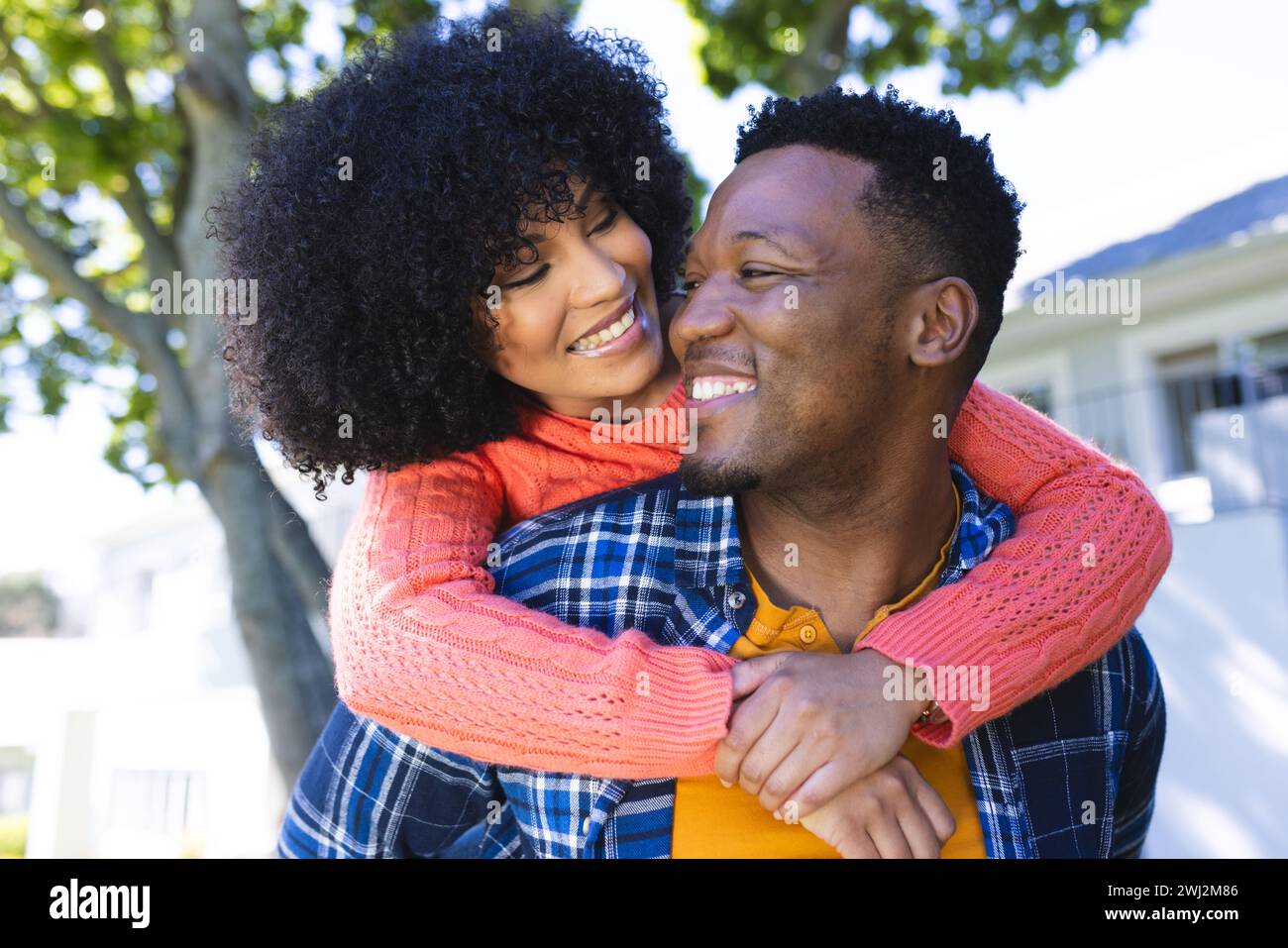 Felice coppia afroamericana che cavalca il piggyback nel giardino soleggiato, spazio fotocopie Foto Stock