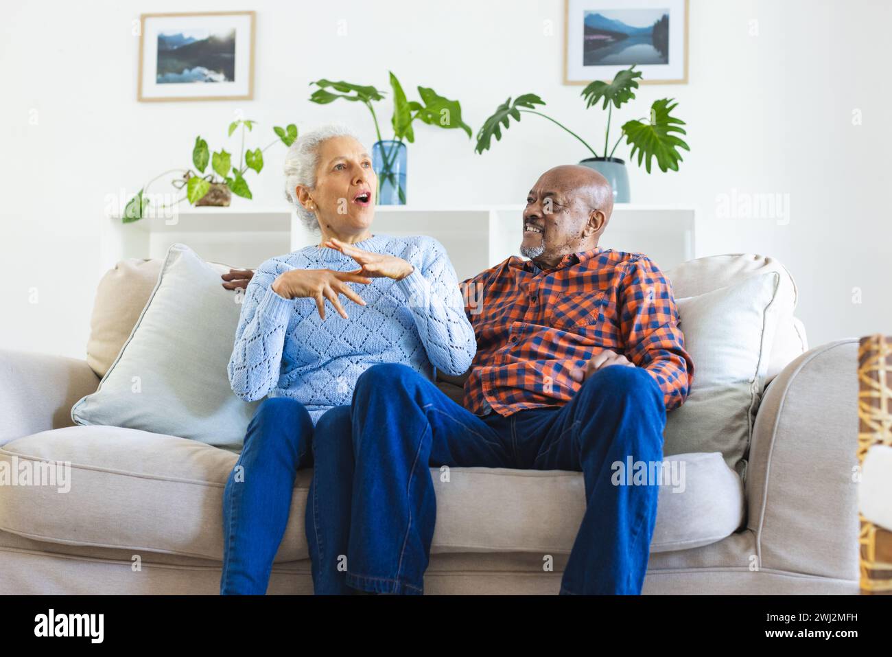 Una coppia di anziani felice e variegata seduto sul divano, parlando e abbracciando il soggiorno soleggiato Foto Stock