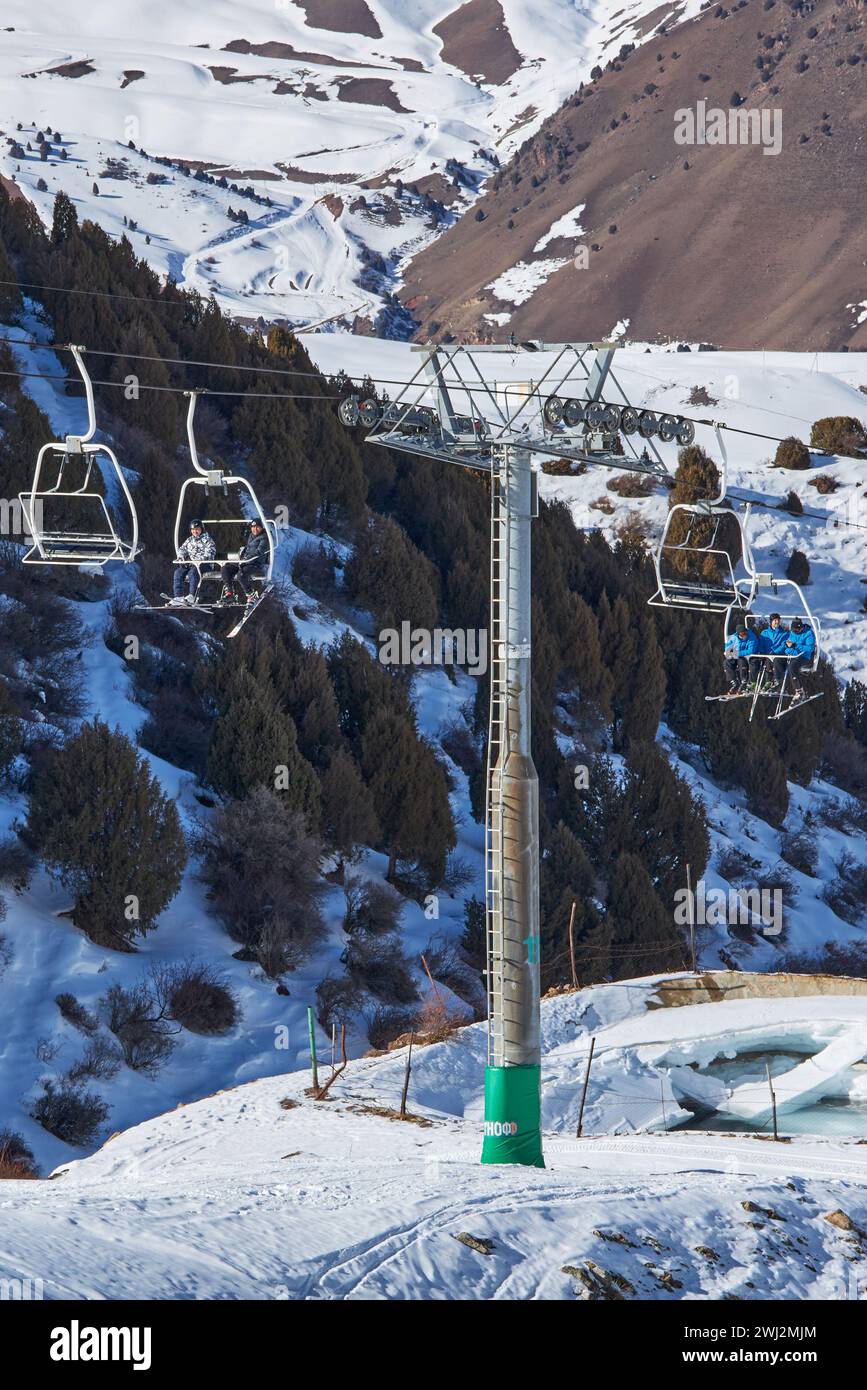 Le persone siedono sulle sedie della funivia che porta alla cima della pista da sci. Palo della funivia, costruzione. Attività per le vacanze invernali, sciatori, snowboarder, festa Foto Stock