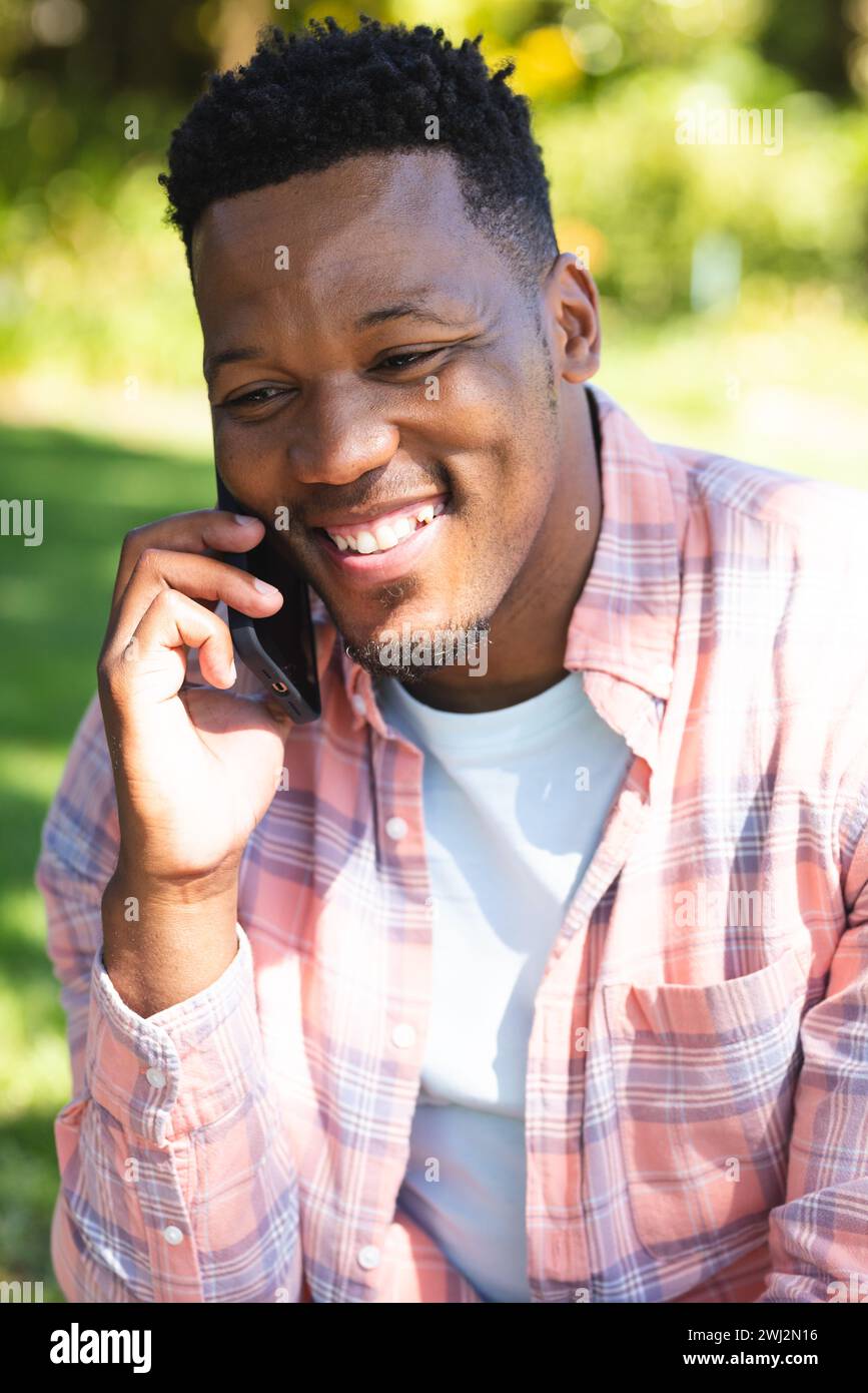 Felice uomo afroamericano seduto sulle scale e a parlare su smartphone nel giardino soleggiato, spazio fotocopie Foto Stock