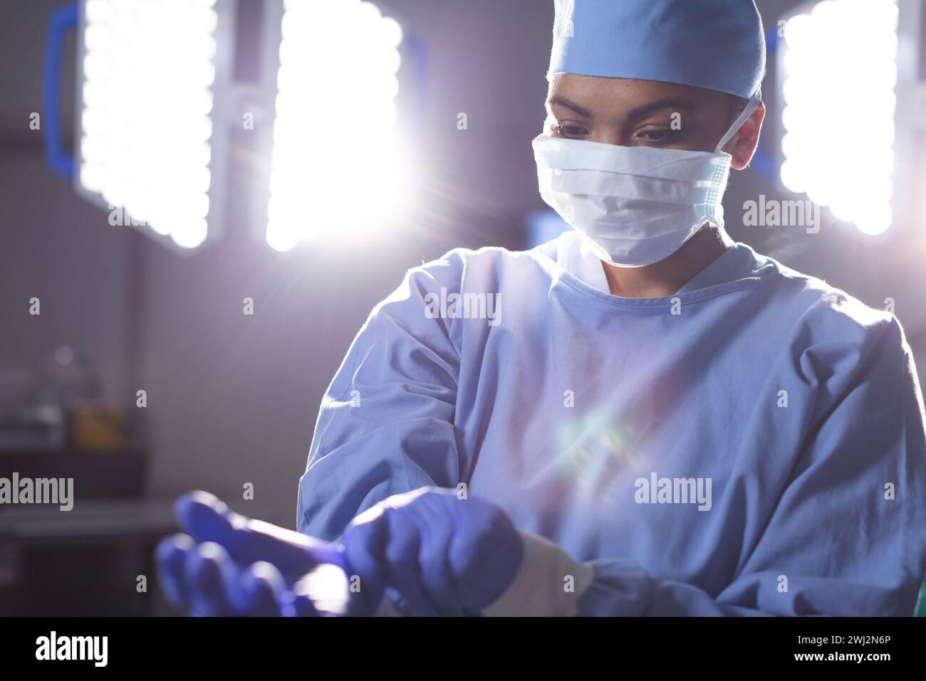 Chirurgo femminile birazziale che indossa camice chirurgico e guanti medici in sala operatoria Foto Stock
