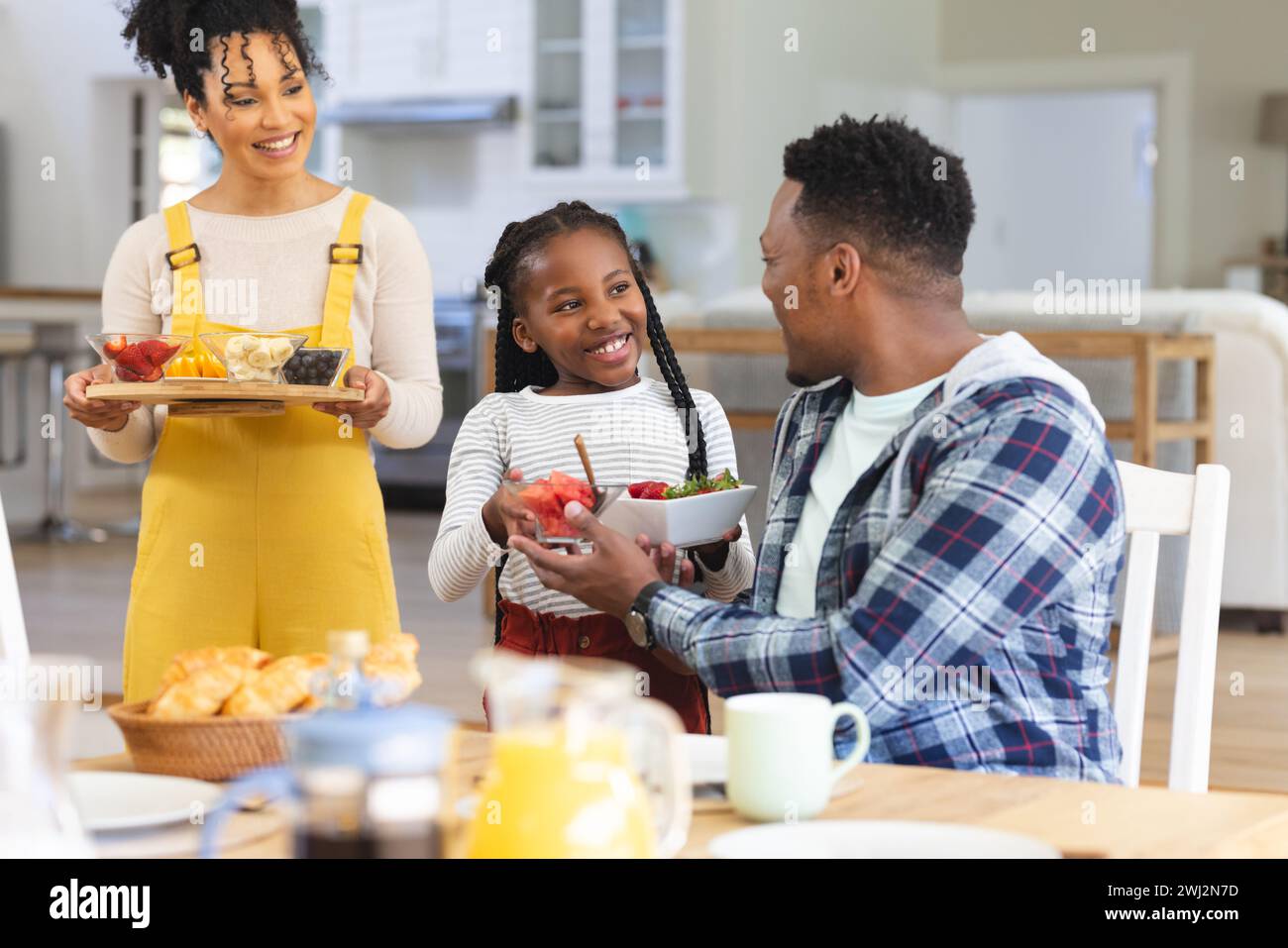 Famiglia afroamericana felice che porta frutta fresca sul tavolo nella sala da pranzo di casa, spazio fotocopie Foto Stock