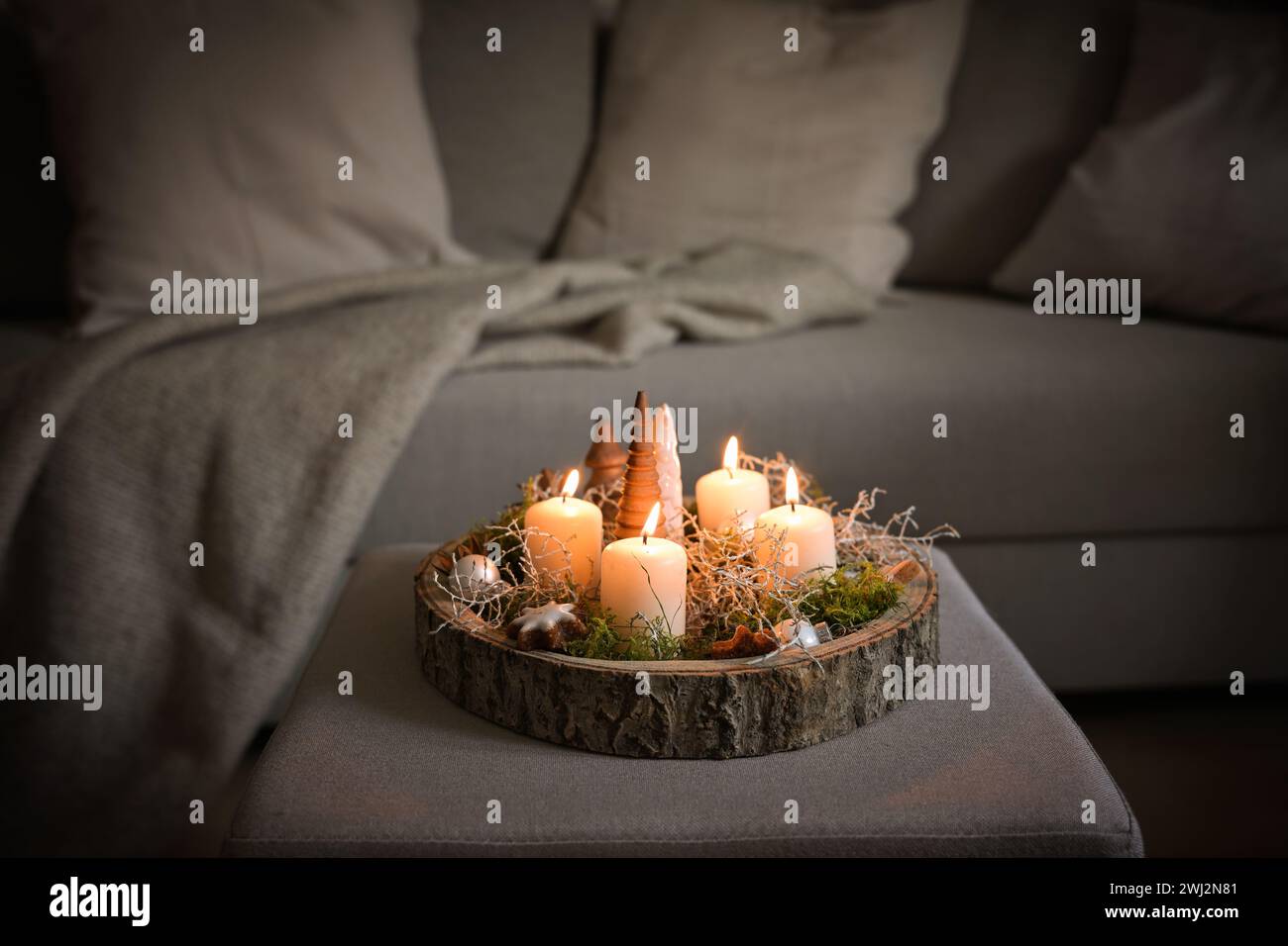 Quattro candele bianche dell'avvento e decorazioni natalizie in un vassoio rustico sull'albero su un ottomano su un divano, un accogliente arredamento per la casa invernale Foto Stock