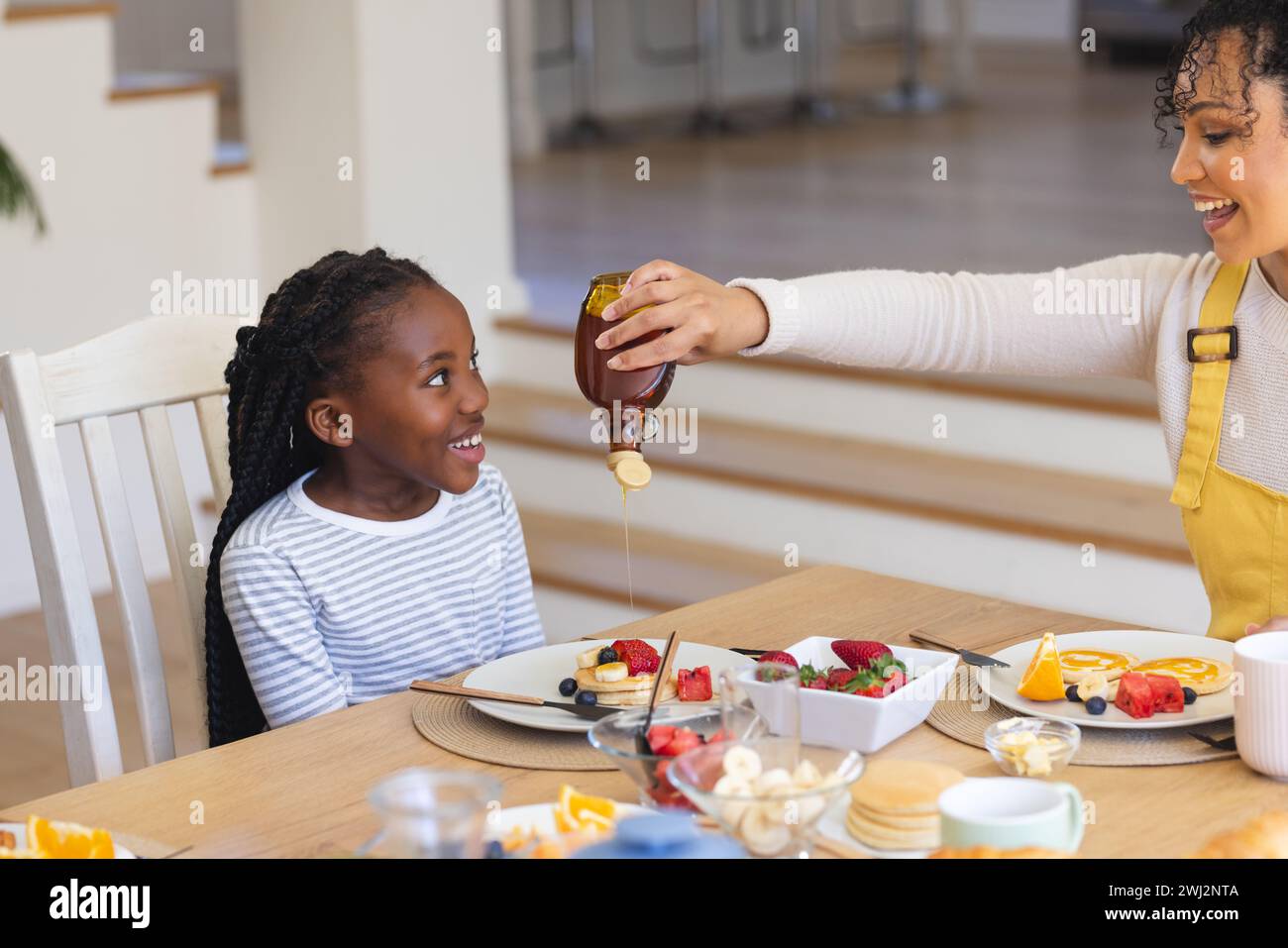Buona madre afroamericana che versa sciroppo d'acero sulla frutta nella sala da pranzo di casa, copia spazio Foto Stock