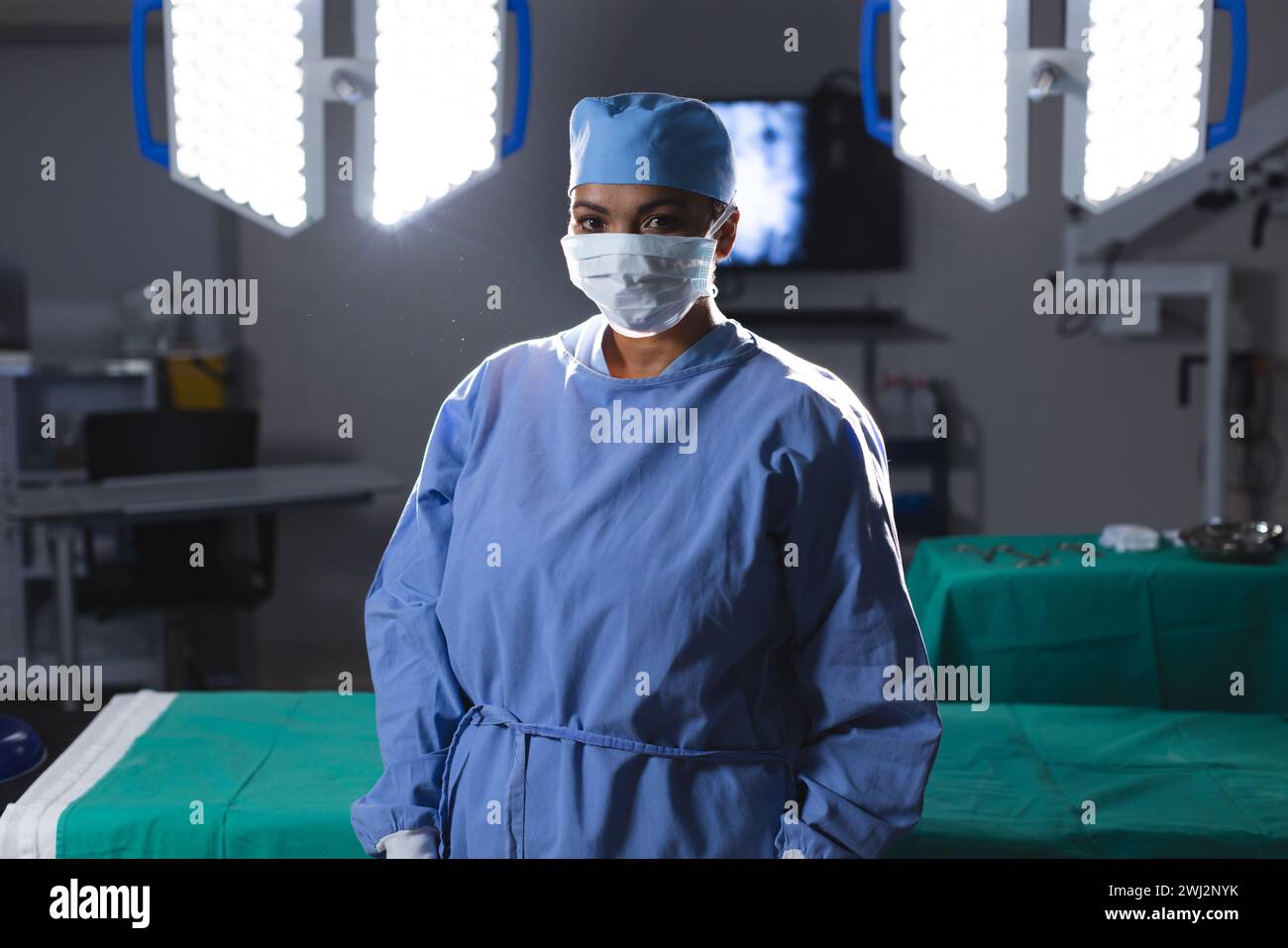 Ritratto di chirurgo birazziale femminile che indossa camice chirurgico e maschera viso in sala operatoria Foto Stock