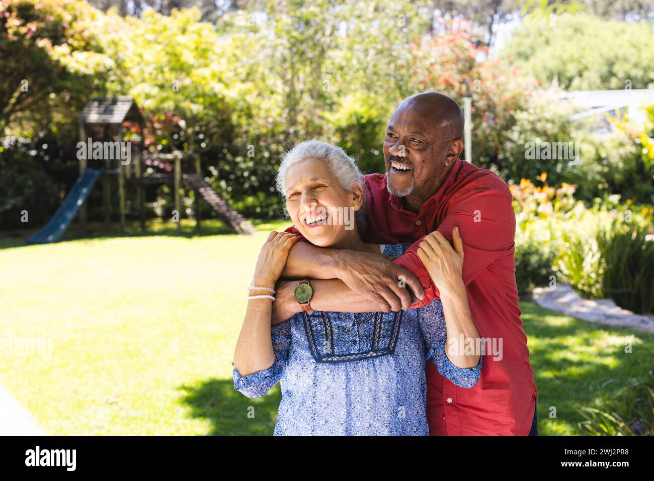 Una coppia di anziani felice e variegata che si abbraccia nel giardino soleggiato Foto Stock