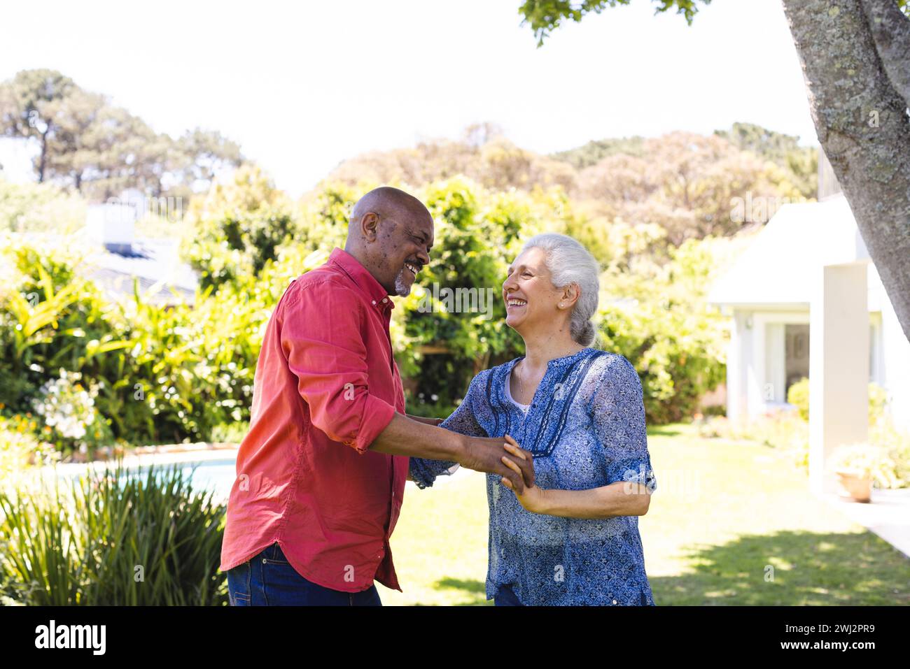 Coppia di anziani felice e variegata che balla nel giardino soleggiato Foto Stock