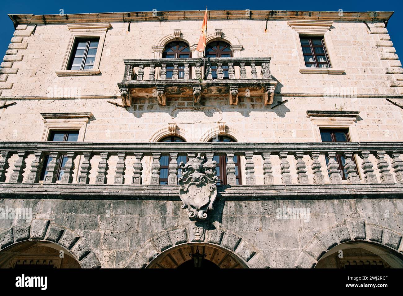 Lo stemma scolpito in pietra è appeso alla terrazza di un antico edificio con una bandiera sventolante Foto Stock