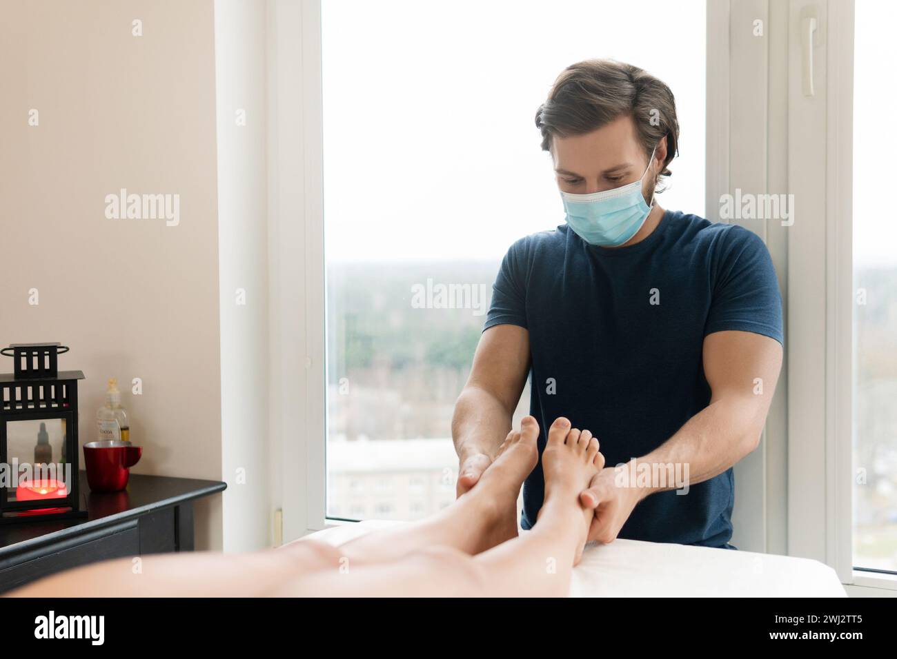 Massaggiatore professionista che indossa una maschera di prevenzione durante il massaggio ai piedi femminile Foto Stock