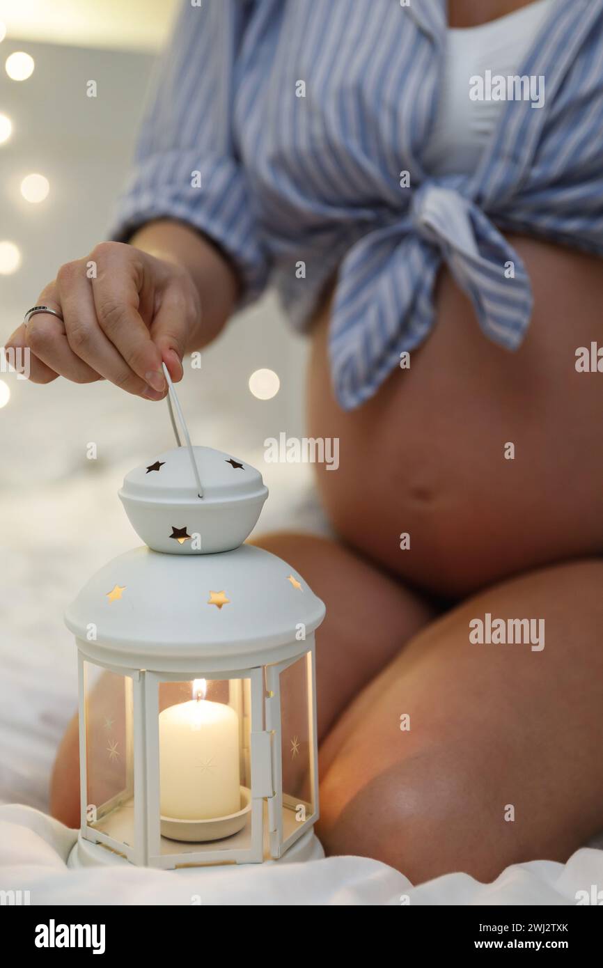 Sensuale donna incinta con la lanterna delle candele nella sua accogliente camera da letto Foto Stock