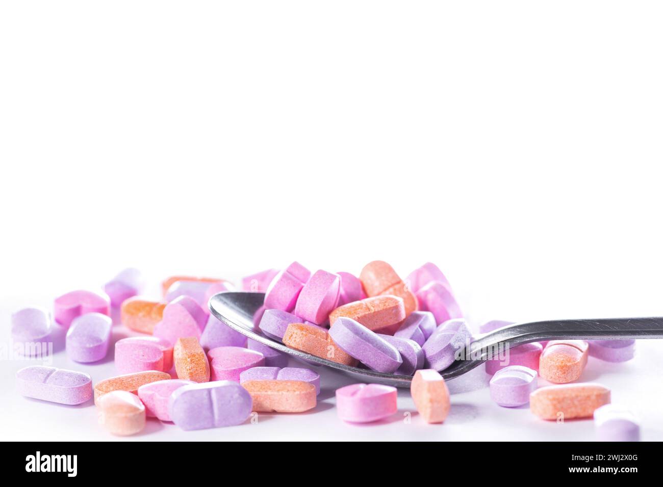Primo piano di cucchiaio e pila di pillole su sfondo bianco. Foto Stock