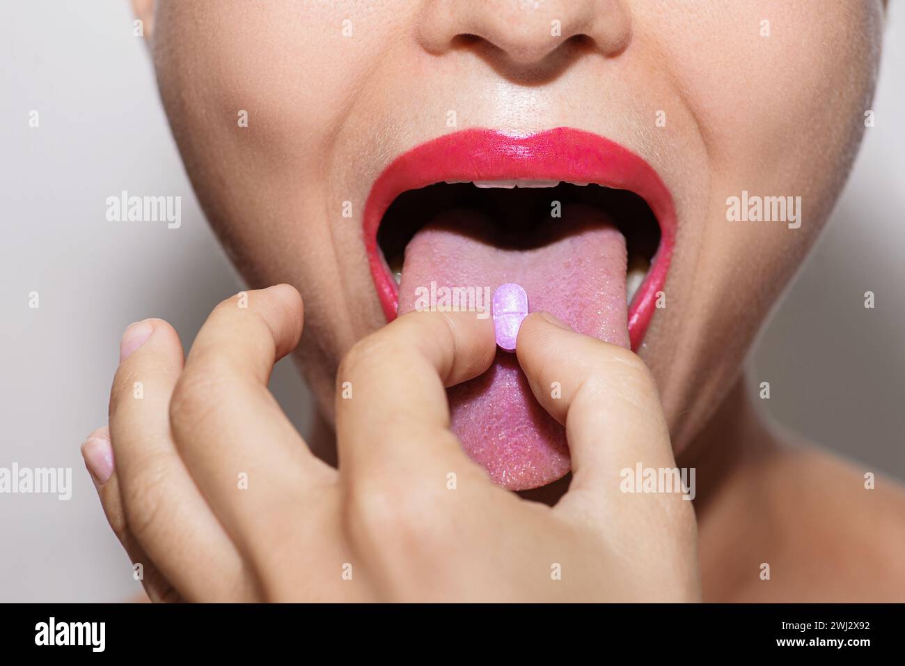 Foto ravvicinata di donna che mette la vitamina viola o pillola di droga sulla lingua Foto Stock