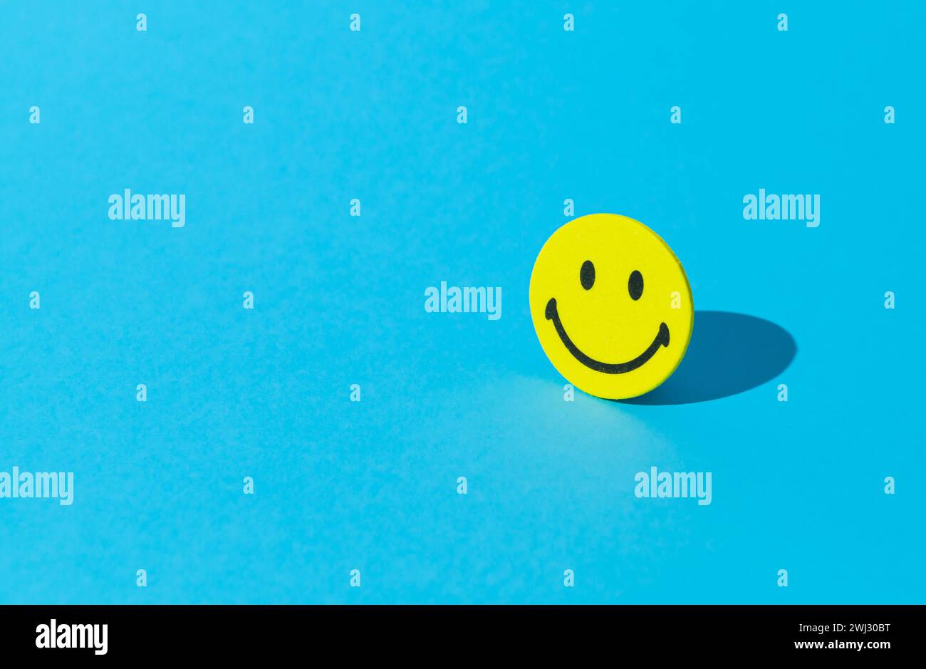 Layout creativo realizzato con adesivo smiley su sfondo blu. Pensiero positivo minimo e concetto di buon umore. Foto Stock