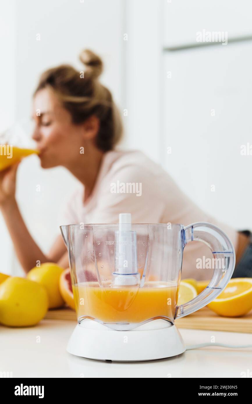 Spremiagrumi e donna che beve succo d'arancia appena spremuto in casa Foto Stock