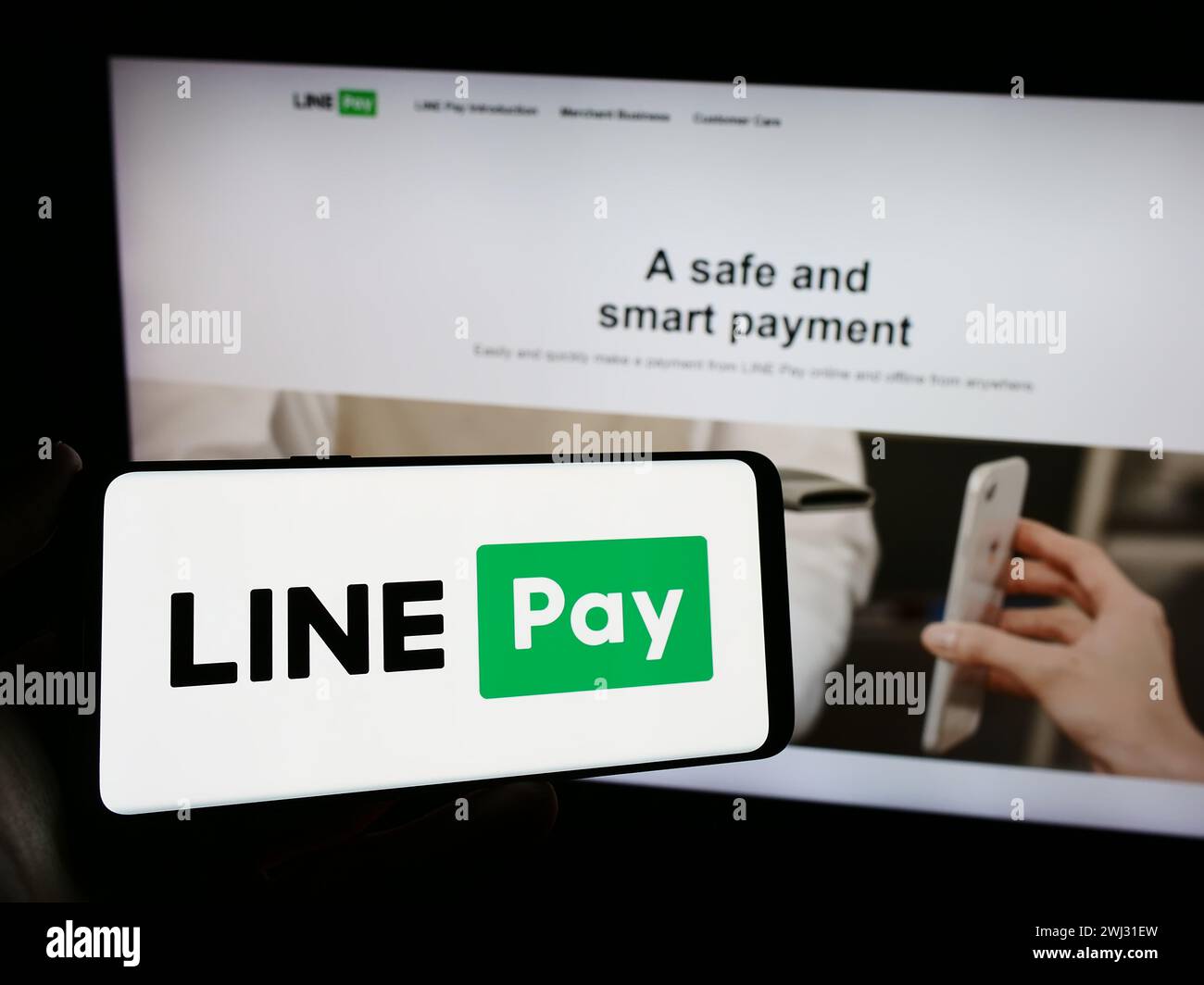 La persona che detiene un cellulare con il logo della società di pagamenti thailandese LINE pay davanti alla pagina web aziendale. Mettere a fuoco il display del telefono. Foto Stock