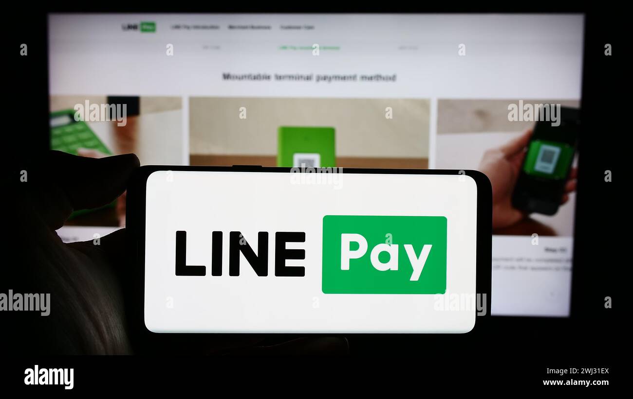 La persona che possiede un telefono cellulare con il logo della società tailandese di pagamento LINE pay davanti alla pagina web aziendale. Mettere a fuoco il display del telefono. Foto Stock