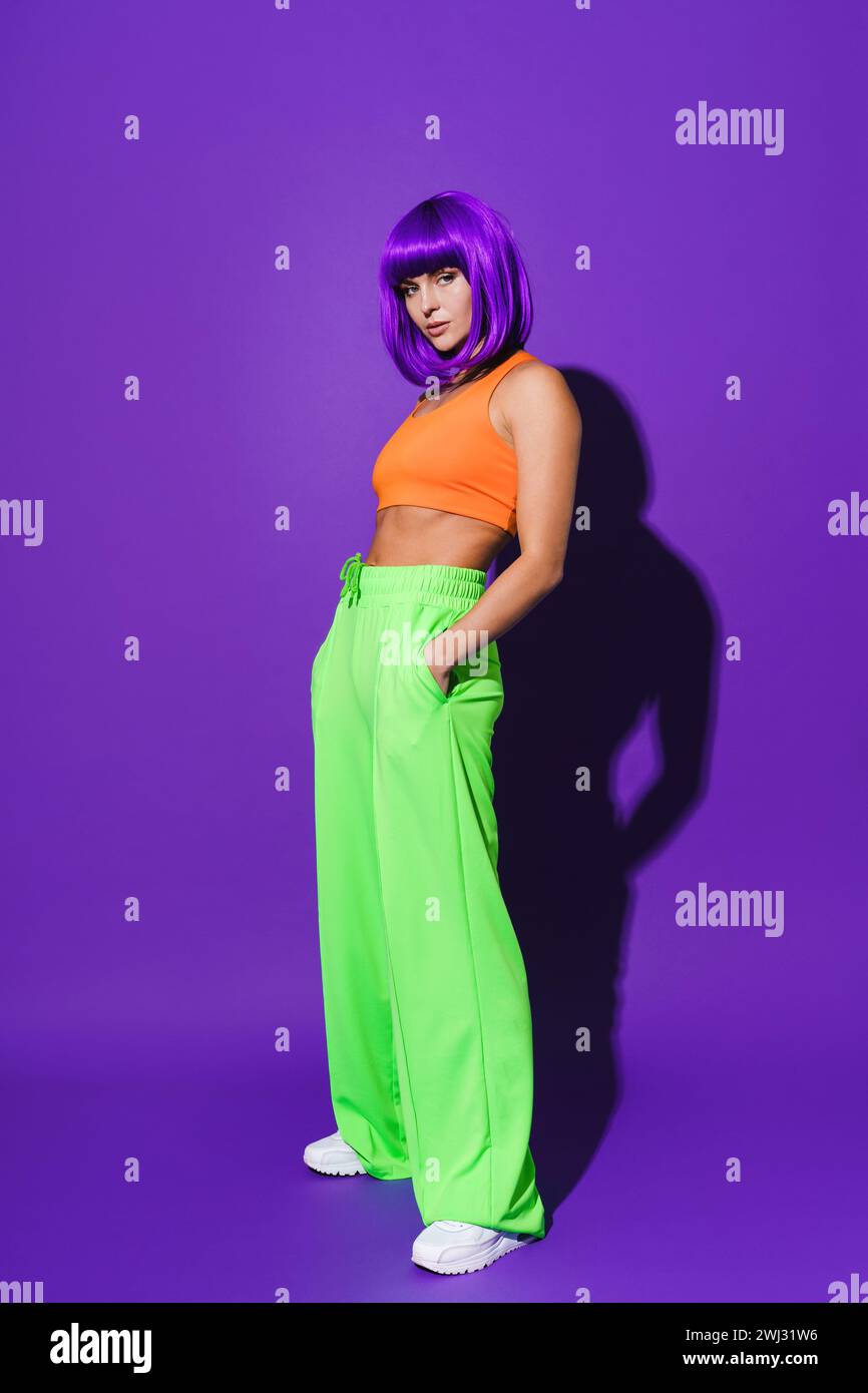 Giovane donna che indossa abbigliamento sportivo colorato su sfondo viola Foto Stock
