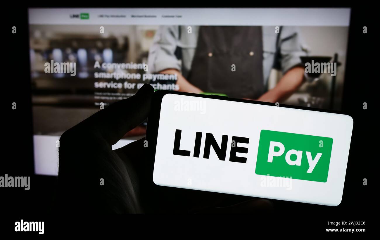 La persona che possiede uno smartphone con il logo della società di pagamenti tailandese LINE pay davanti al sito web. Mettere a fuoco il display del telefono. Foto Stock