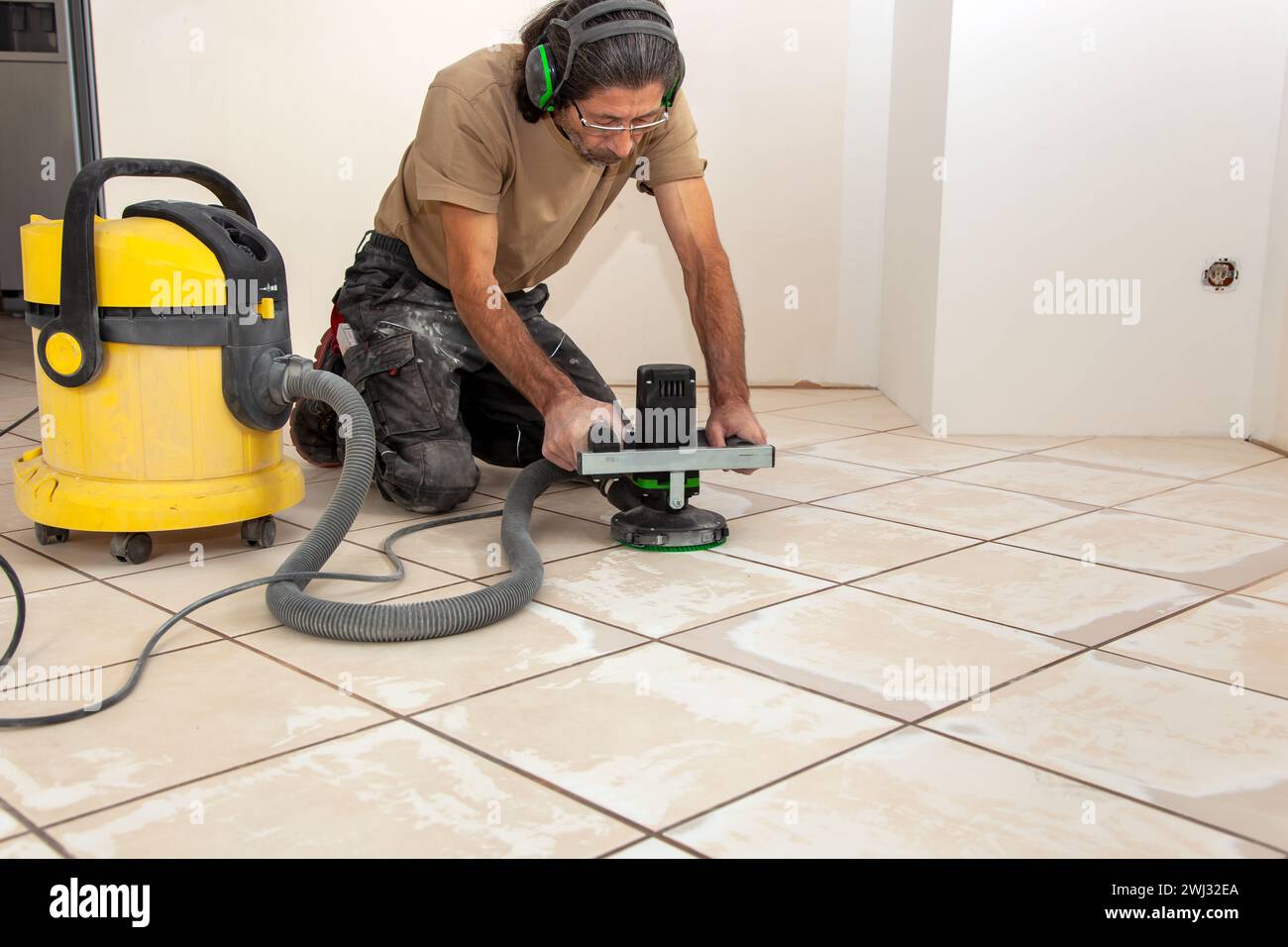 L'uomo sta lavorando con un Grinder. Levigatura di pavimenti piastrelle con rettificatrice elettrica per pavimenti Foto Stock