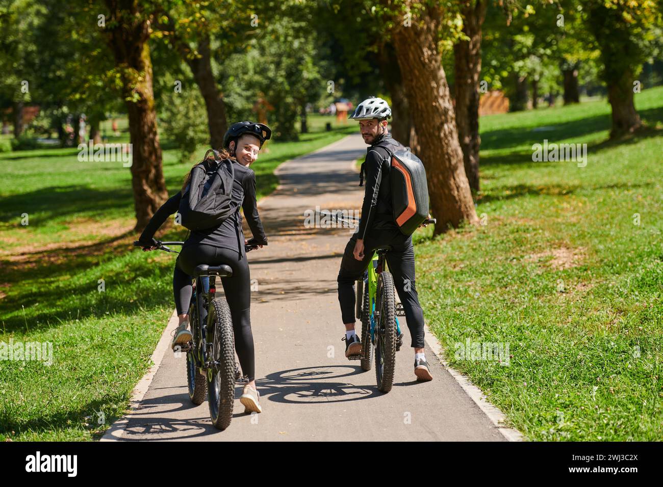 Una coppia beata, adornata di attrezzatura da ciclismo professionale, gode di una romantica corsa in bicicletta attraverso un parco, circondato dalla moderna nat Foto Stock