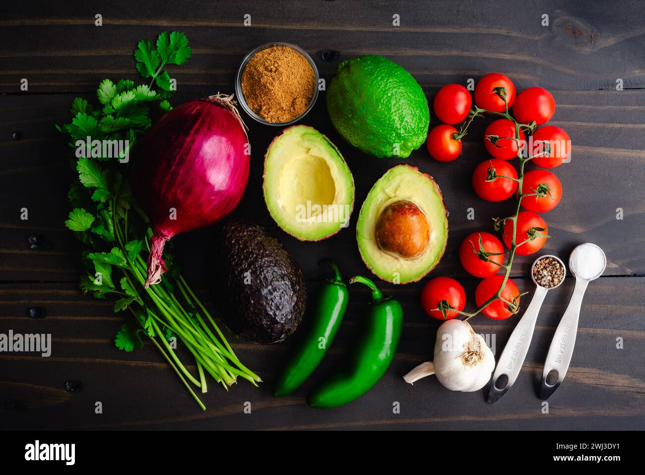 Ingredienti guacamole freschi su un tavolo in legno rustico: Avocado Haas, limes, coriandolo e altri ingredienti per un tuffo guacamole su sfondo scuro Foto Stock