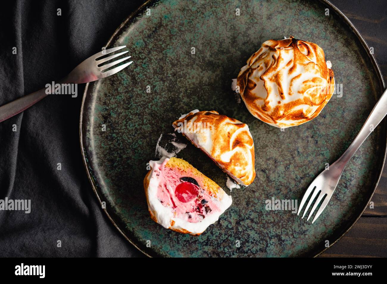 Mini dessert dell'Alaska al forno con Forks on a Dark Plate: Porzioni singole intere e dimezzate di gelato, torta e dessert di meringa dell'Alaska Foto Stock