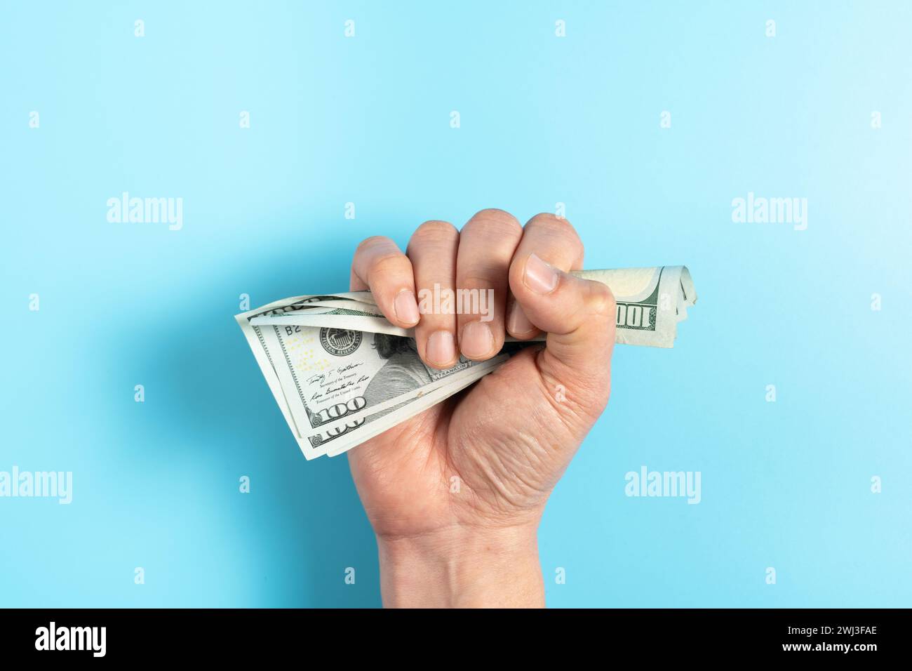 Una mano in un pugno che spreme soldi da cento dollari di banconote Foto Stock