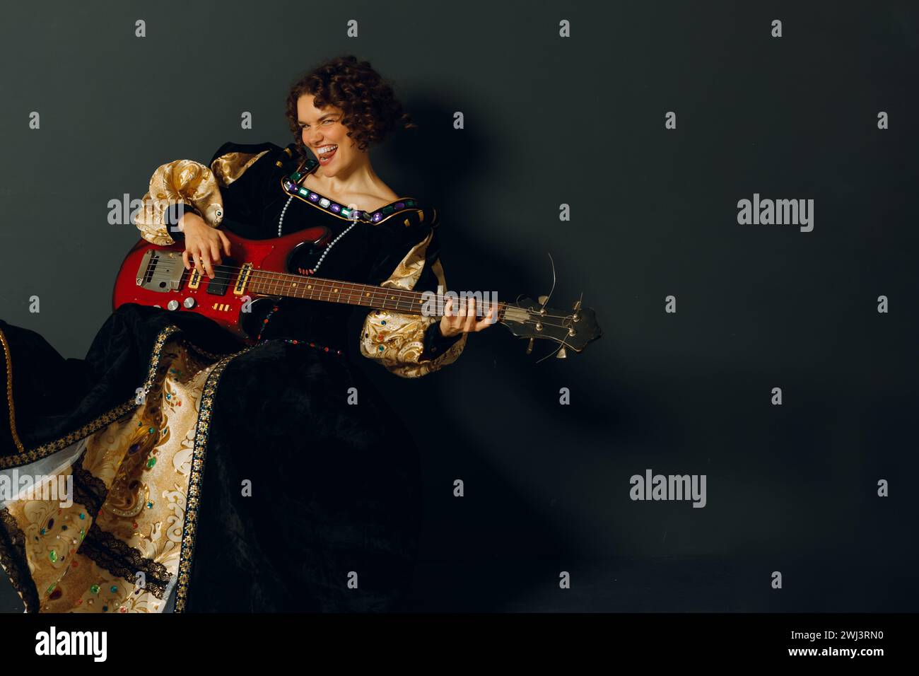 Ritratto di una giovane donna adulta che suona musica rock con la chitarra elettrica e indossa un abito medievale. Foto Stock