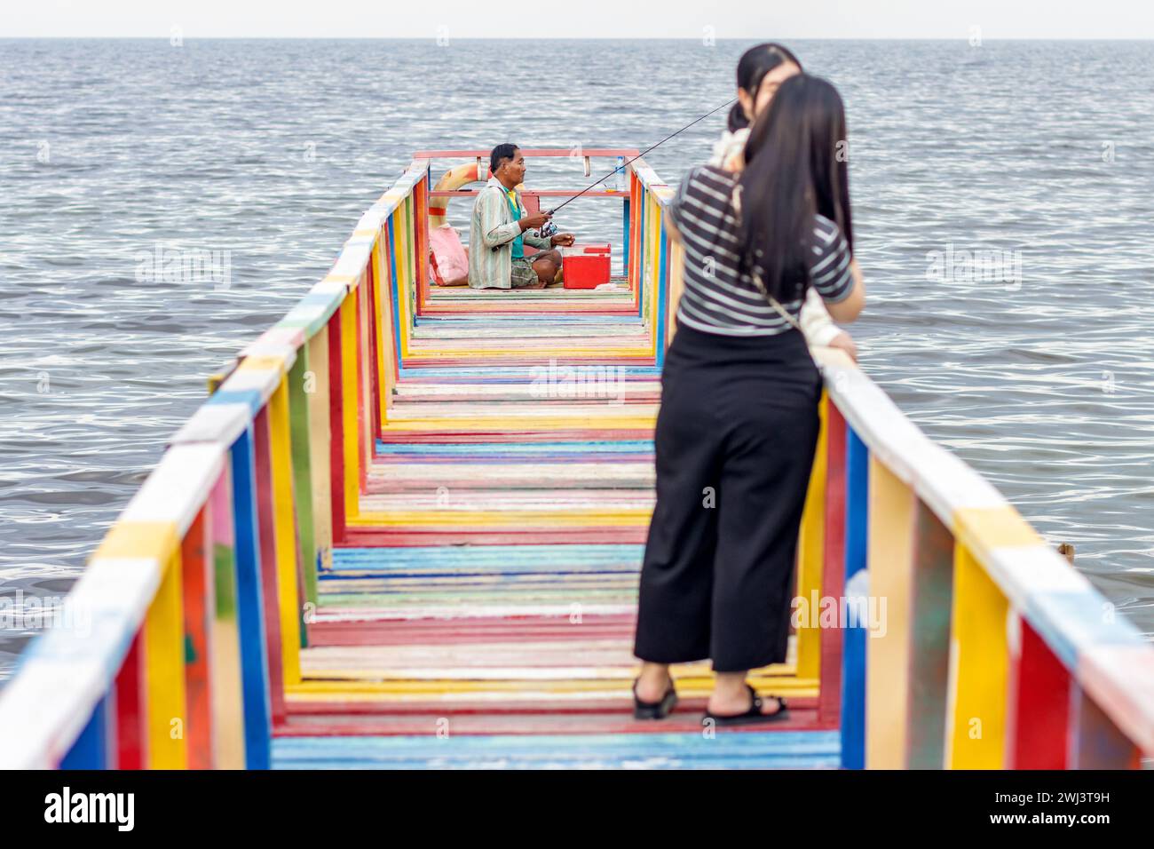 Le ragazze scattano foto su una passerella colorata alla fine della quale un pescatore Foto Stock