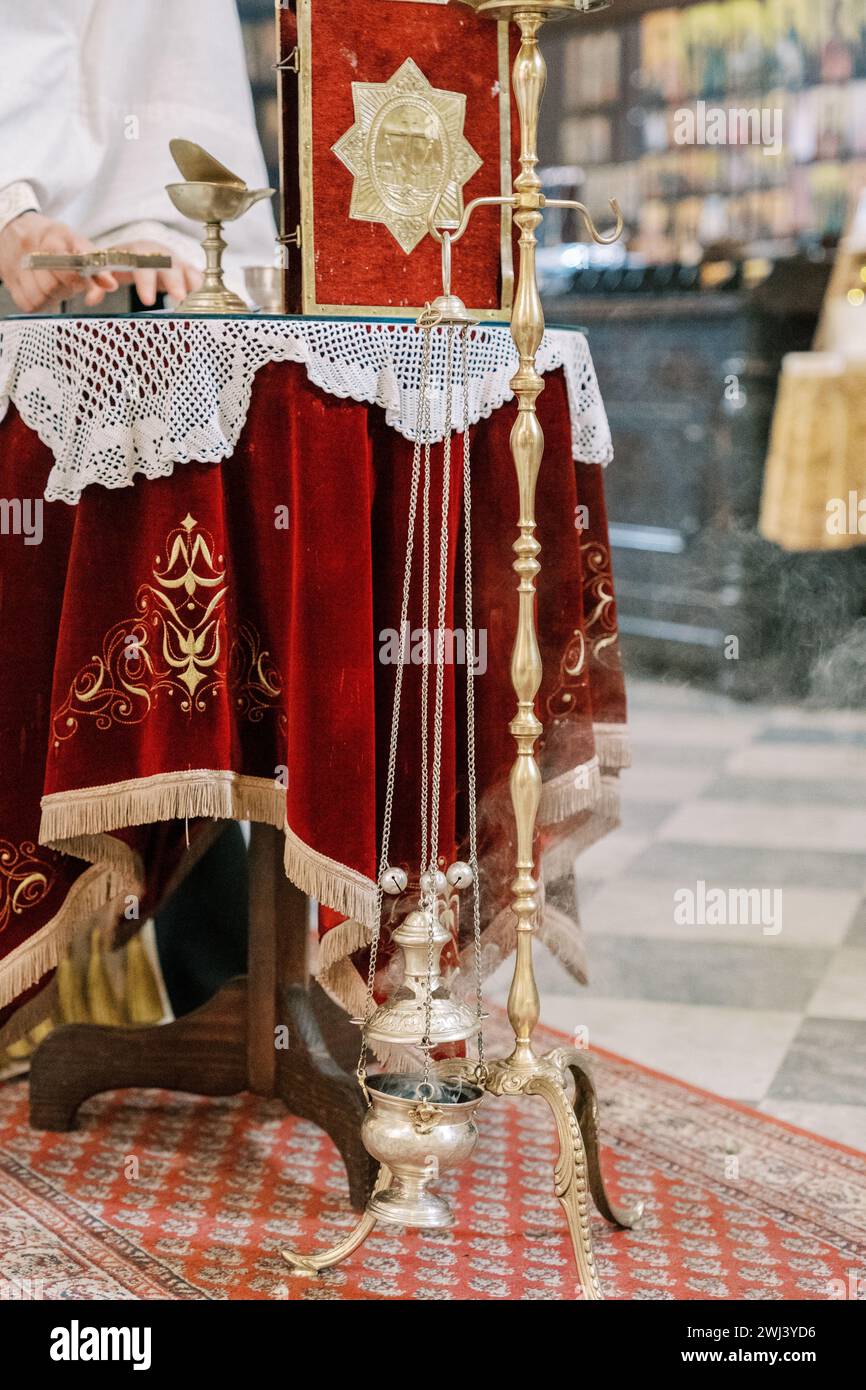Il prete mette la croce sul tavolo accanto al censore che fuma su una tribuna. Ritagliato. Senza volto Foto Stock