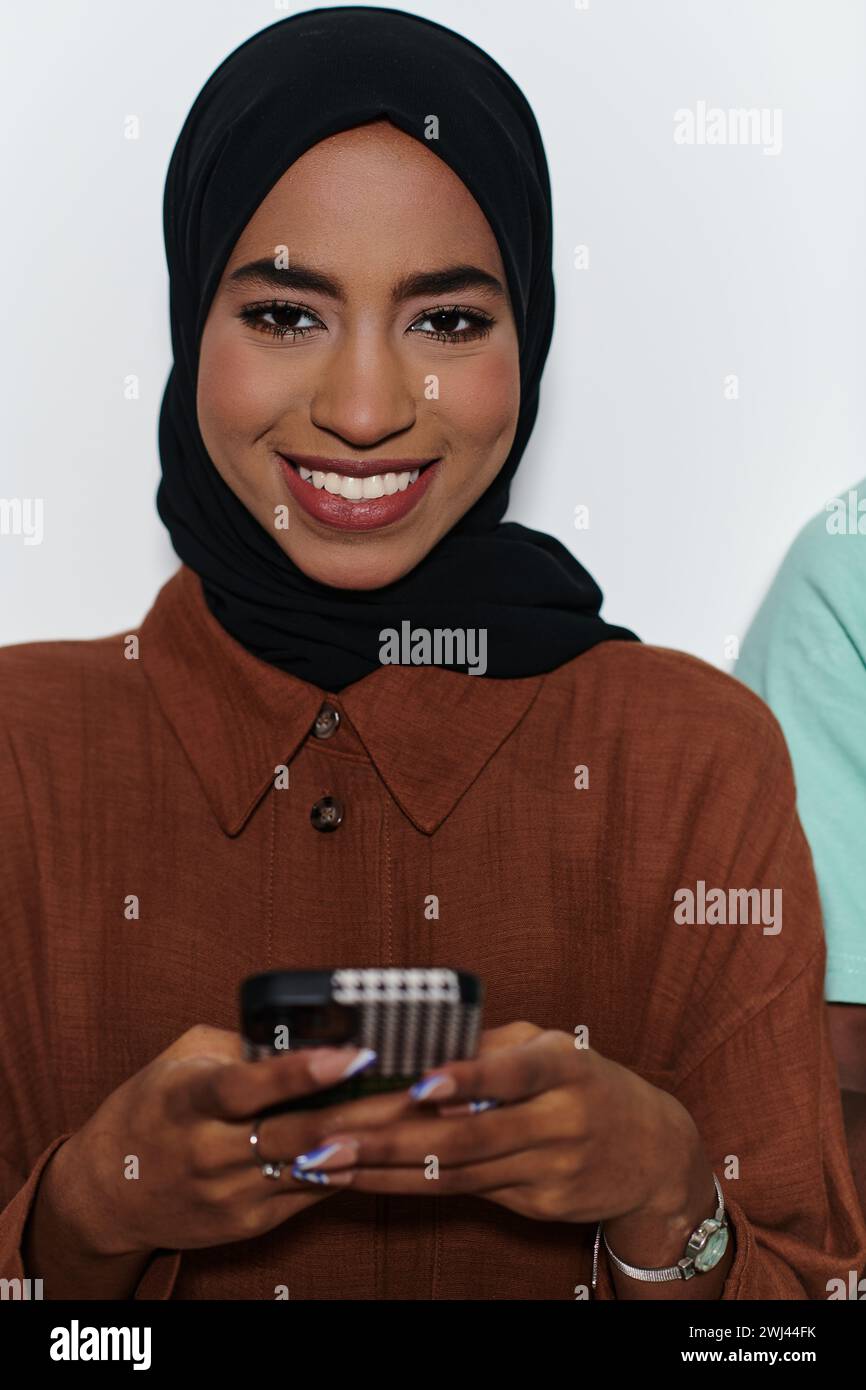 Un'elegante donna araba, adornata in un hijab, si impegna con la modernità mentre utilizza uno smartphone, la giustapposizione di att tradizionali Foto Stock