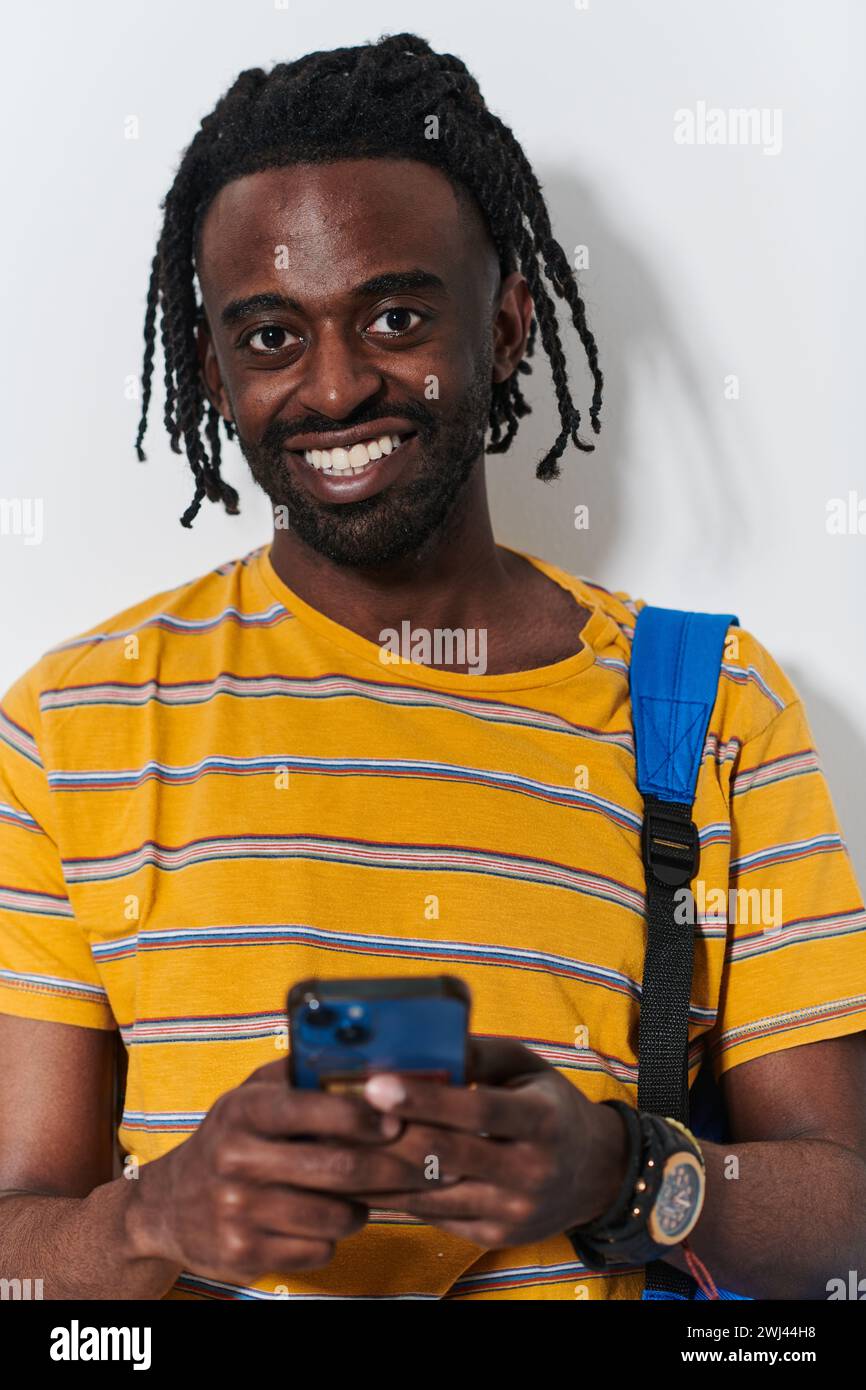 Un adolescente afroamericano si impegna con il suo smartphone su uno sfondo bianco incontaminato, incapsulando l'essenza del contempo Foto Stock