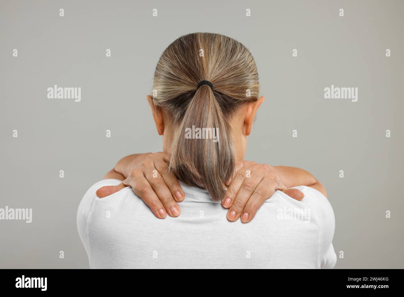 Donna matura che soffre di dolore al collo su sfondo grigio, vista posteriore Foto Stock