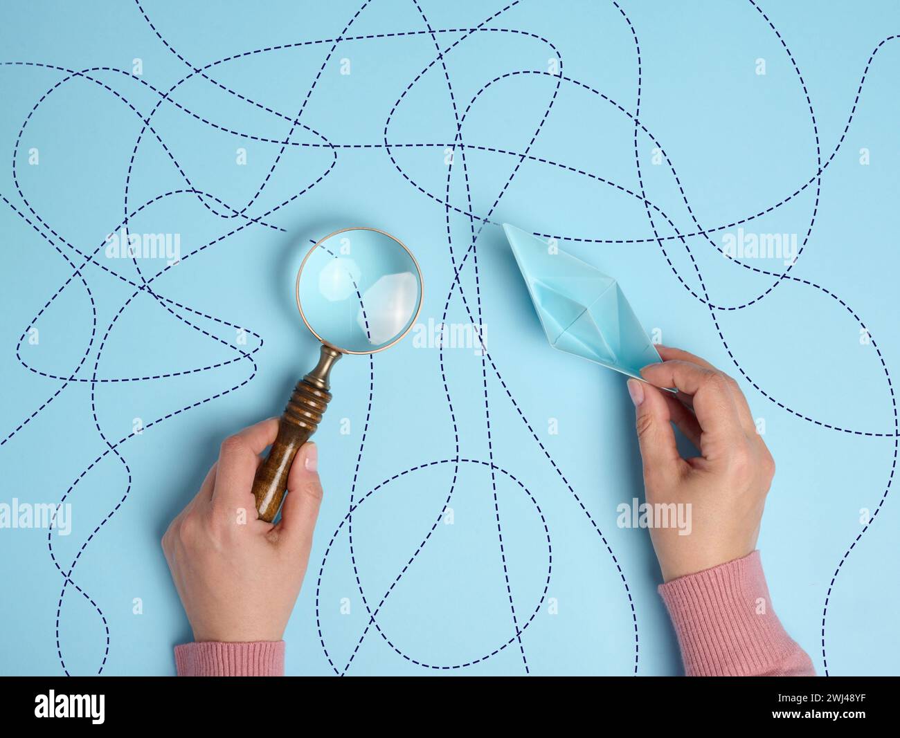 Una mano femminile regge una barca di carta e una lente d'ingrandimento, simboleggiando l'esplorazione del percorso Foto Stock