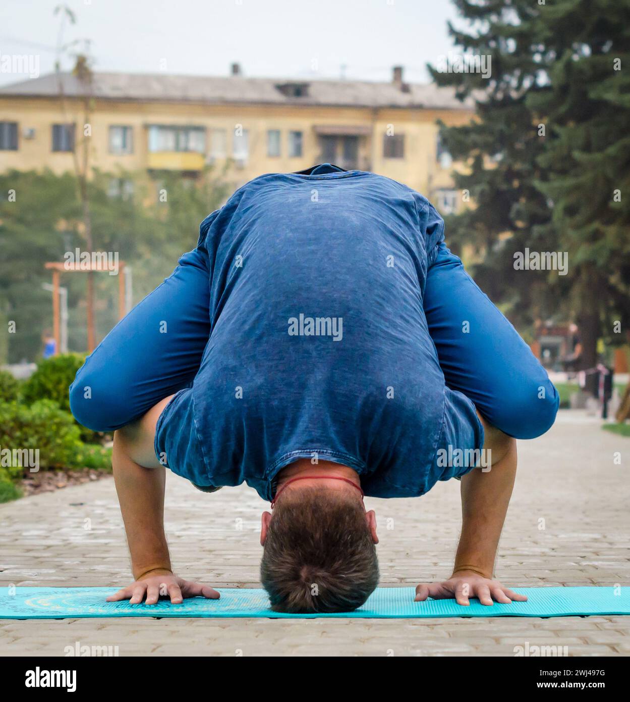 Giovane in yoga posa sul tappeto sul marciapiede sullo sfondo della strada della città Foto Stock