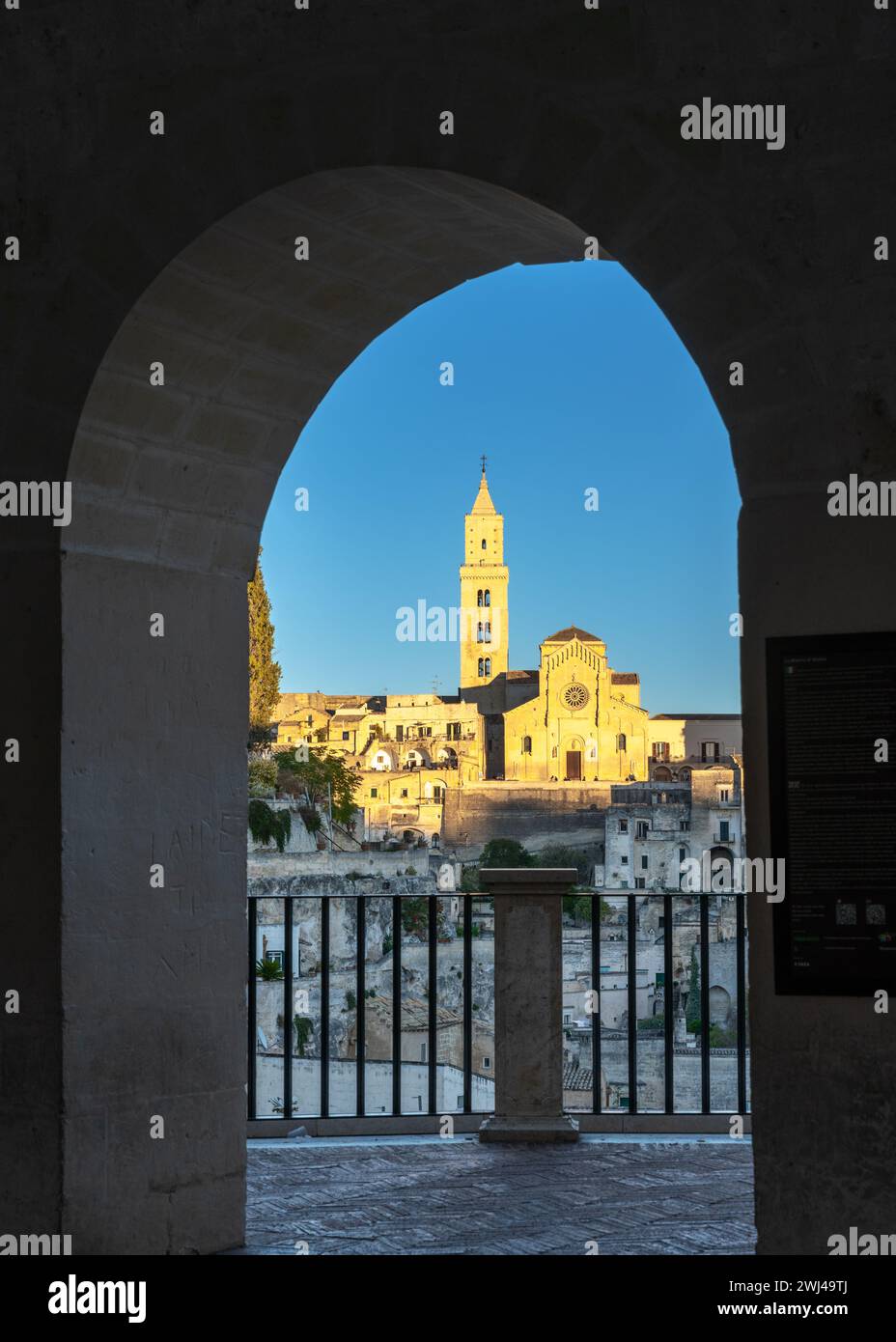 Vista della storica cattedrale di Matera attraverso un arco in pietra della città vecchia negli ultimi raggi del sole Foto Stock