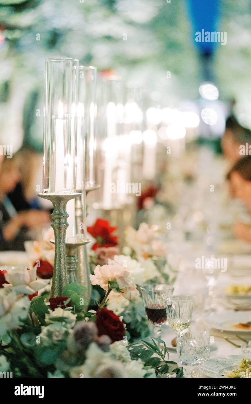 Candele brucianti su candelabri con tappi di vetro si stagliano su un tavolo festivo tra i fiori Foto Stock