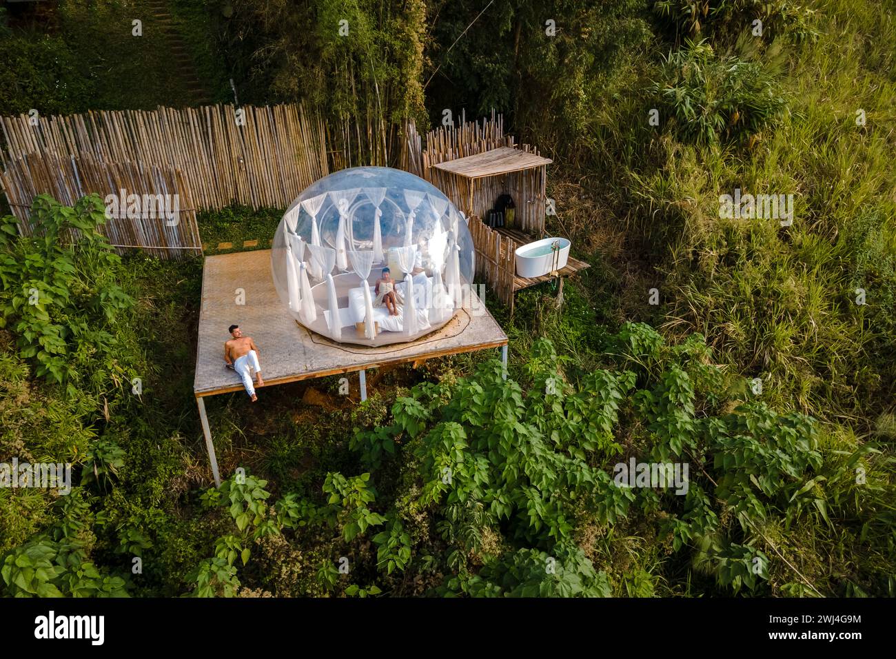 Coppia uomo e donna in una tenda a bolle d'aria con bagno esterno con vasca nella foresta pluviale Foto Stock