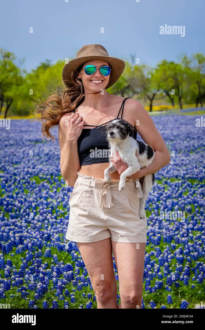 Un'adorabile bruna modella posa in Un campo di fiori Bluebonnet con il suo cane in Un Texas Prarie Foto Stock