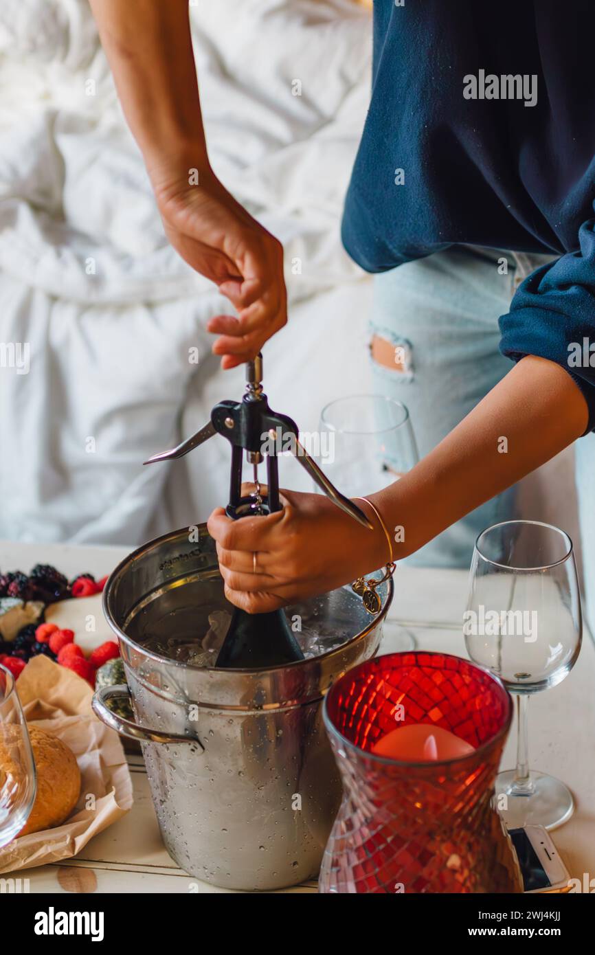 donna che apre una bottiglia di vino freddo nel secchiello dello champagne sul tavolino da caffè con spuntino Foto Stock