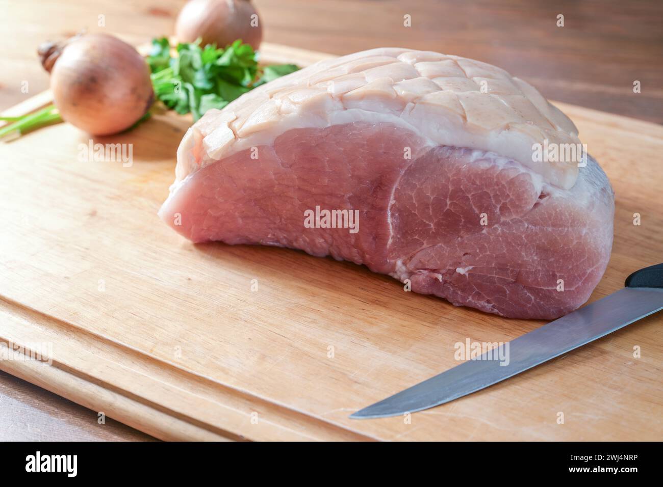 Arrosto di maiale crudo salato su un tagliere di legno con coltello da cucina, cipolle ed erbe aromatiche, preparazione per una festa natalizia Foto Stock