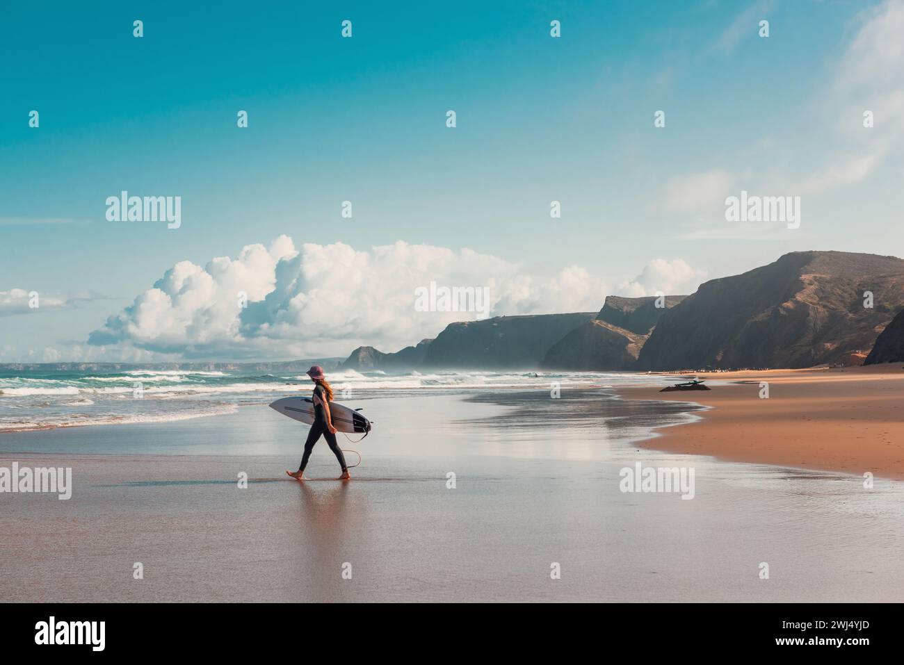 Giovane surfista che cammina nell'Oceano Atlantico sulla spiaggia sabbiosa del Portogallo Foto Stock