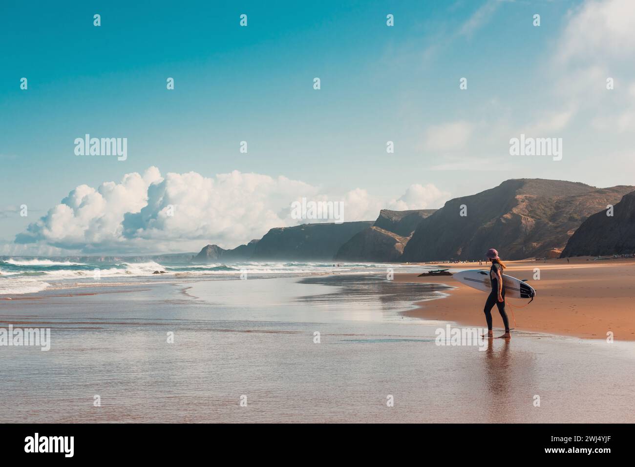 Giovane surfista che cammina nell'Oceano Atlantico sulla spiaggia sabbiosa del Portogallo Foto Stock