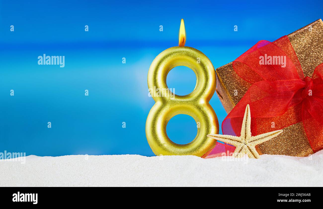 Candela d'oro numero 8 con omaggio con arco rosso e stelle marine sulla spiaggia. 8 marzo, giornata internazionale della donna, compleanno. Copia spazio Foto Stock