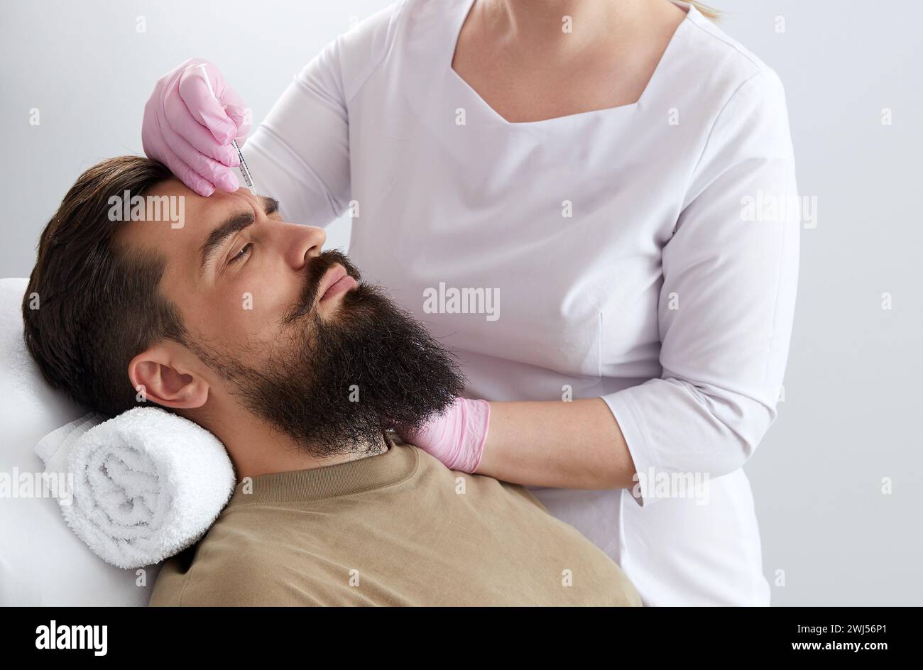 Primo piano dell'uomo bearded che ottiene l'iniezione di bellezza alla clinica estetica. Medico che inietta il riempitivo anti-invecchiamento nel bel viso maschile Foto Stock