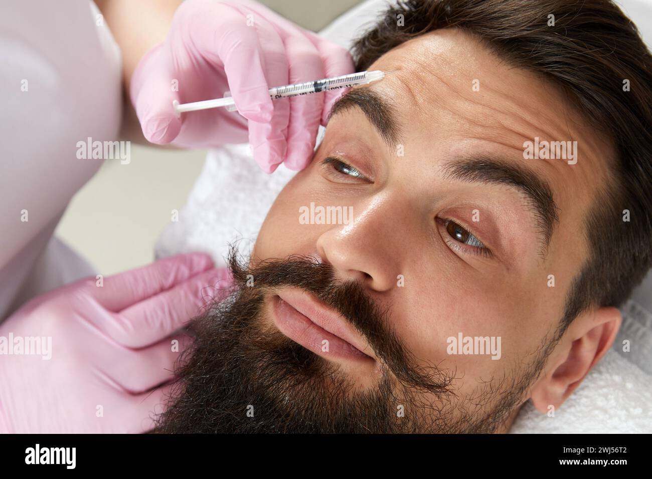 Primo piano dell'uomo bearded che ottiene l'iniezione di bellezza alla clinica estetica. Medico che inietta il riempitivo anti-invecchiamento nel bel viso maschile Foto Stock